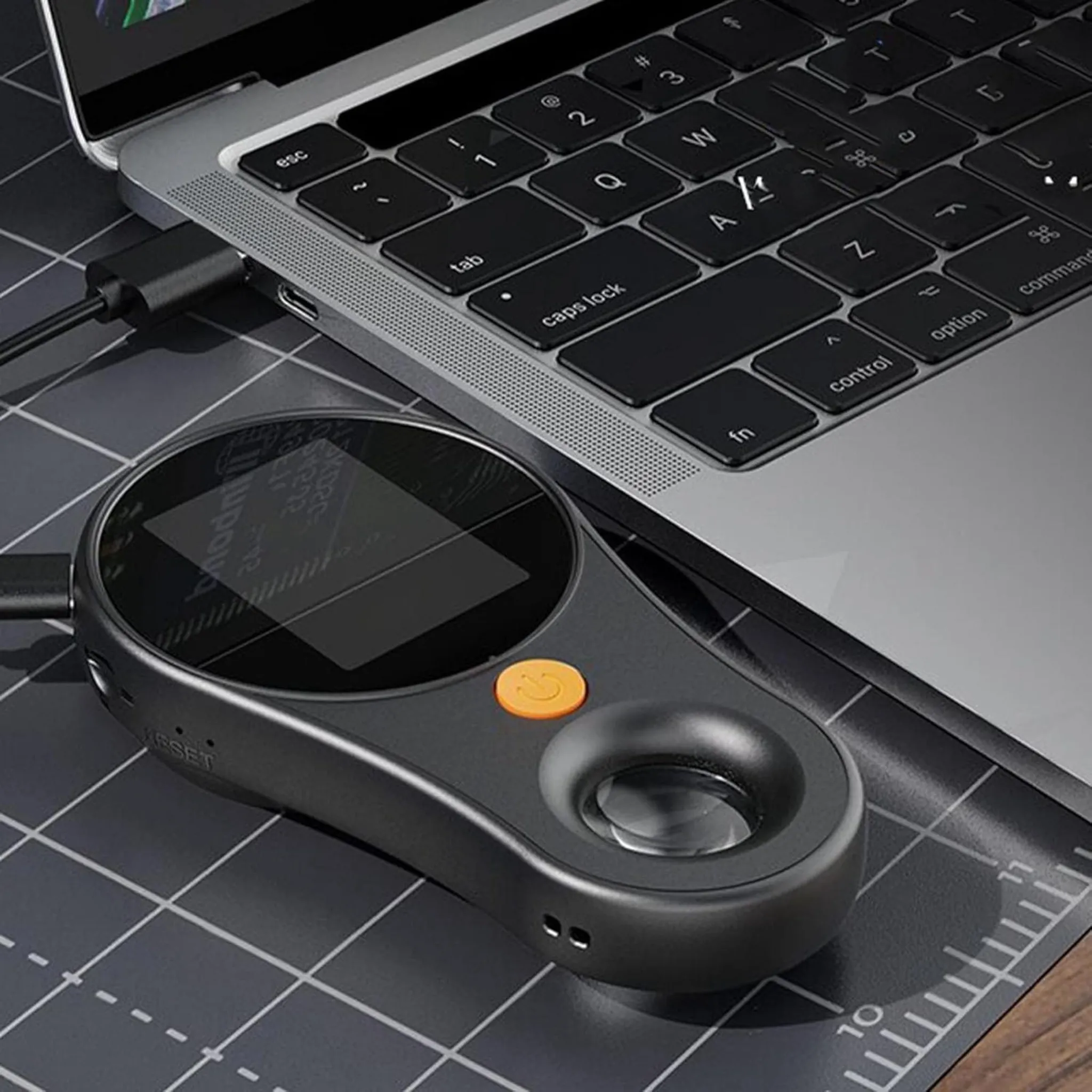 Ein schwarzes Gerät mit Bildschirm und orangefarbenem Knopf neben einem Laptop.