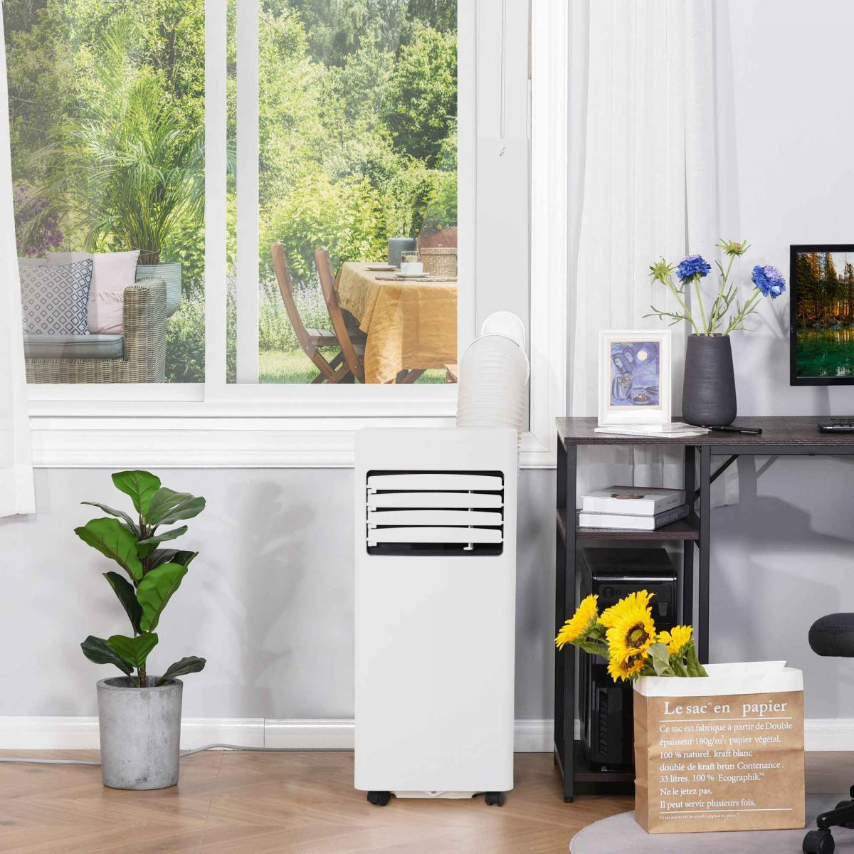 Ein weißer tragbarer Klimaanlage steht neben einem Fenster mit Gartenblick.