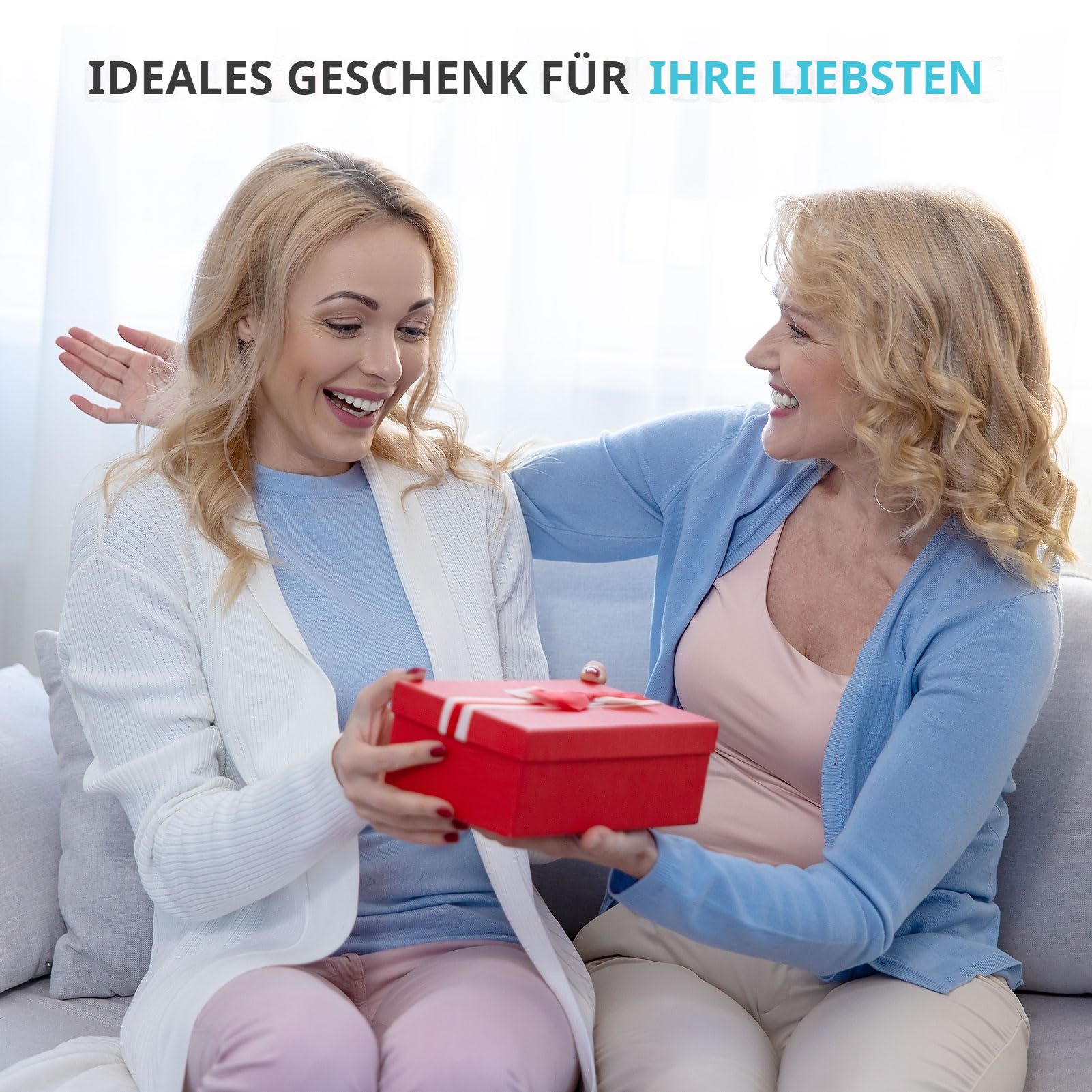 Zwei lachende Frauen sitzen auf einem Sofa und tauschen ein rotes Geschenk aus.