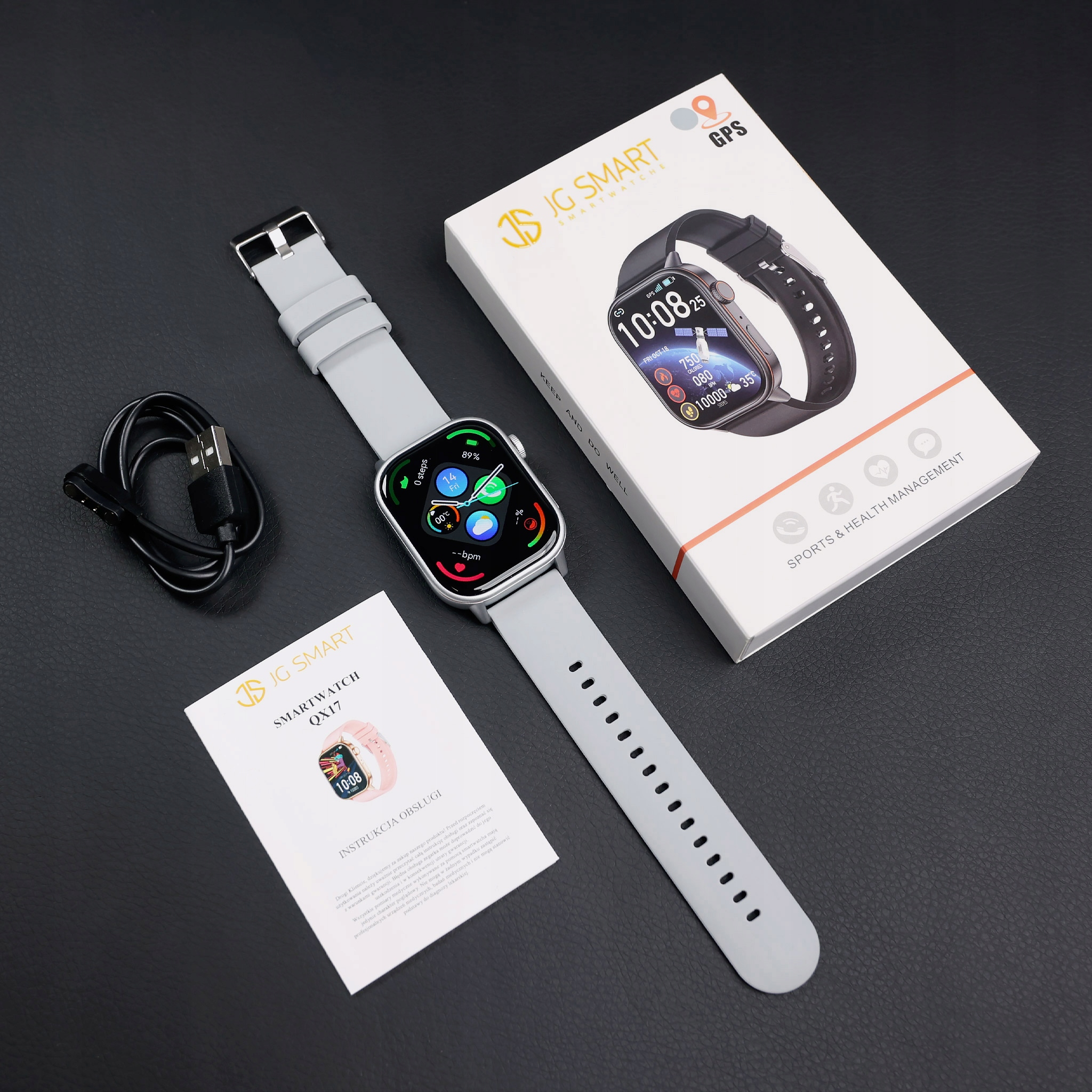 Szara smartwatch z ładowarką i instrukcją na czarnym tle.