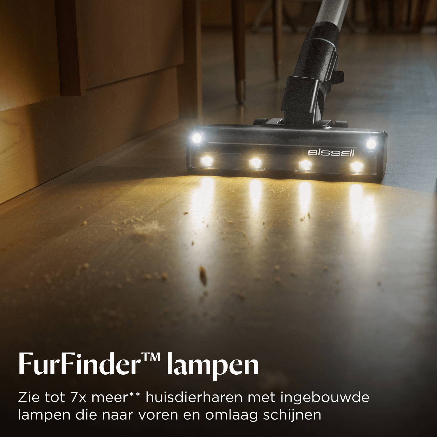 A vacuum cleaner head with lights cleans a wooden floor with debris on it.