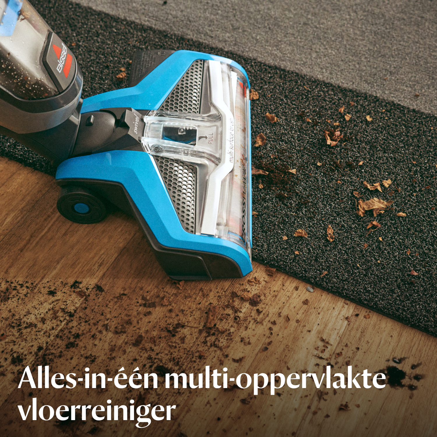 Ein blauer Staubsauger reinigt einen Holzboden und eine dunkle Matte von Schmutz.