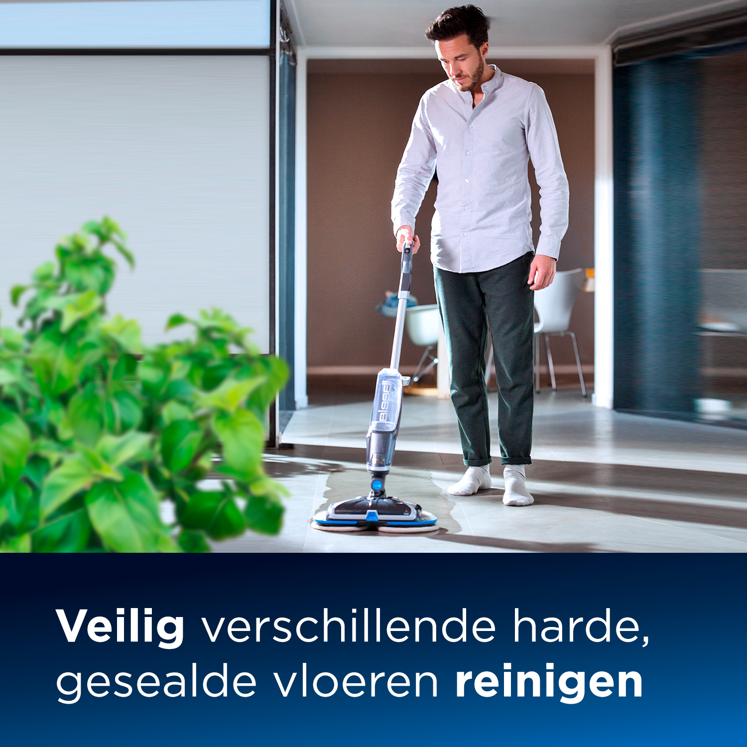 Mann wischt mit einem Nassreiniger über einen Hartboden. Pflanze im Vordergrund.