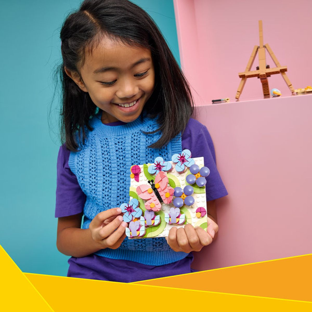 Una niña sostiene un cuadro de flores y mariposas hecho de piezas de Lego.