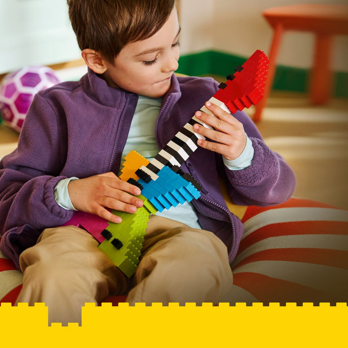 Un bambino suona una colorata chitarra LEGO fatta di mattoncini.