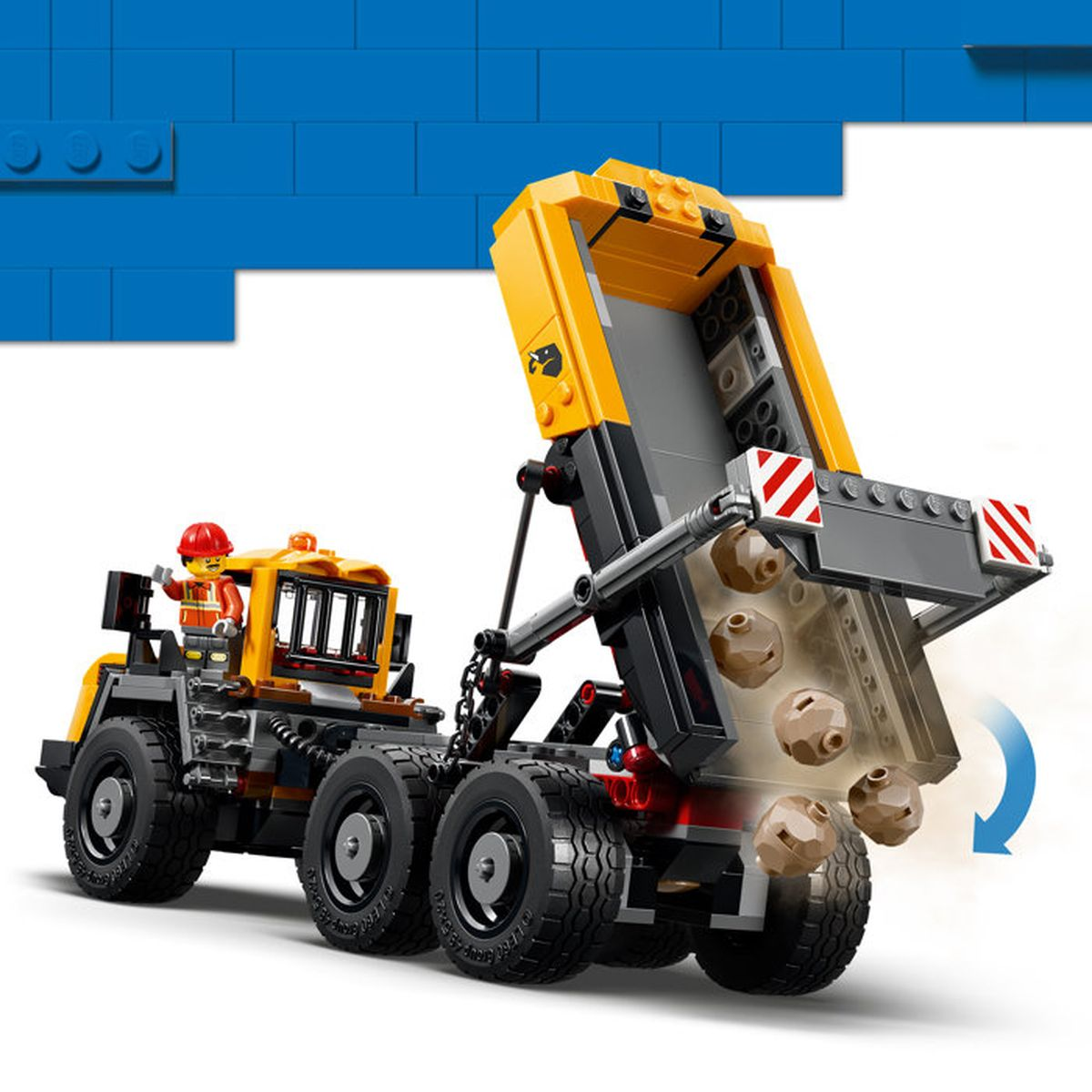 Un camion dumper Lego giallo con un conducente rovescia rocce marroni dal cassone.