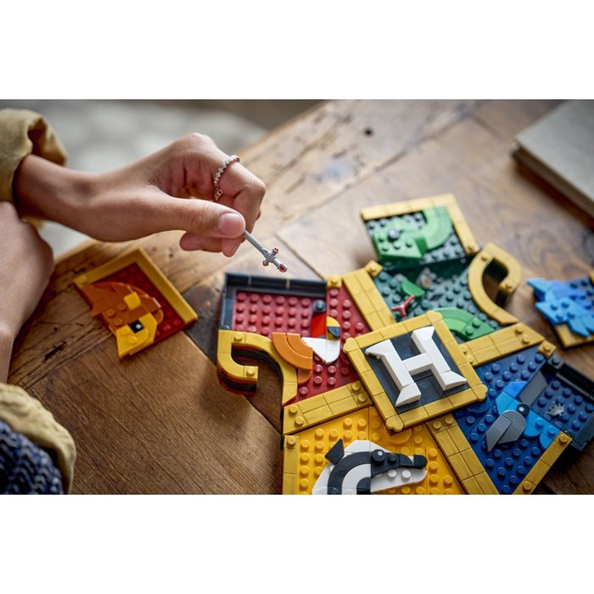 Una mano tiene una piccola spada sopra gli stemmi LEGO di Hogwarts con elementi di animali e lettere.