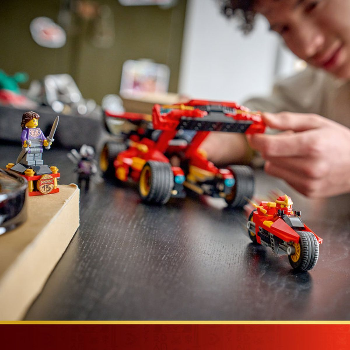 Un niño juega con coches y figuras rojas de Lego en una mesa de madera.