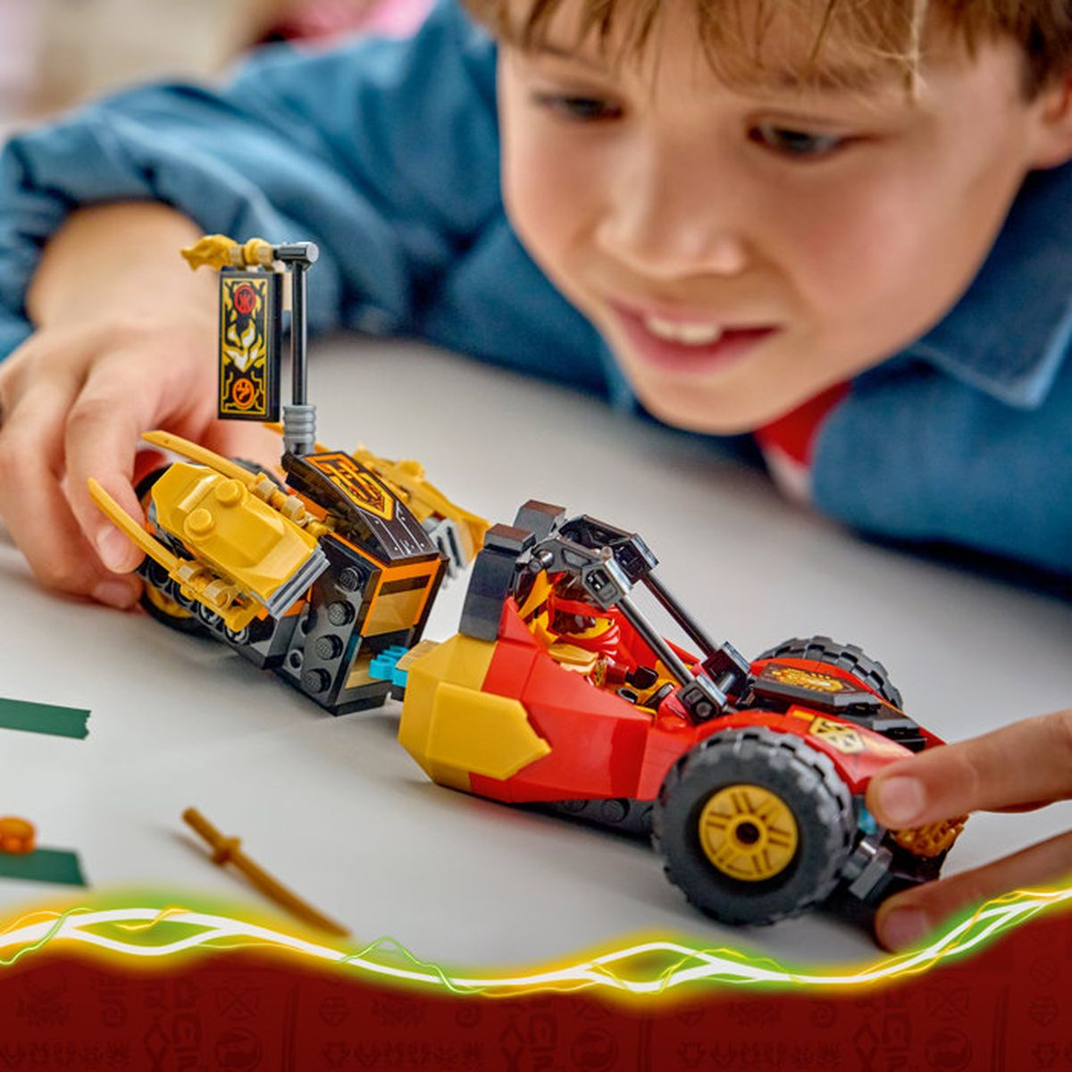 Un niño juega con coches Lego rojos y amarillos en una mesa.