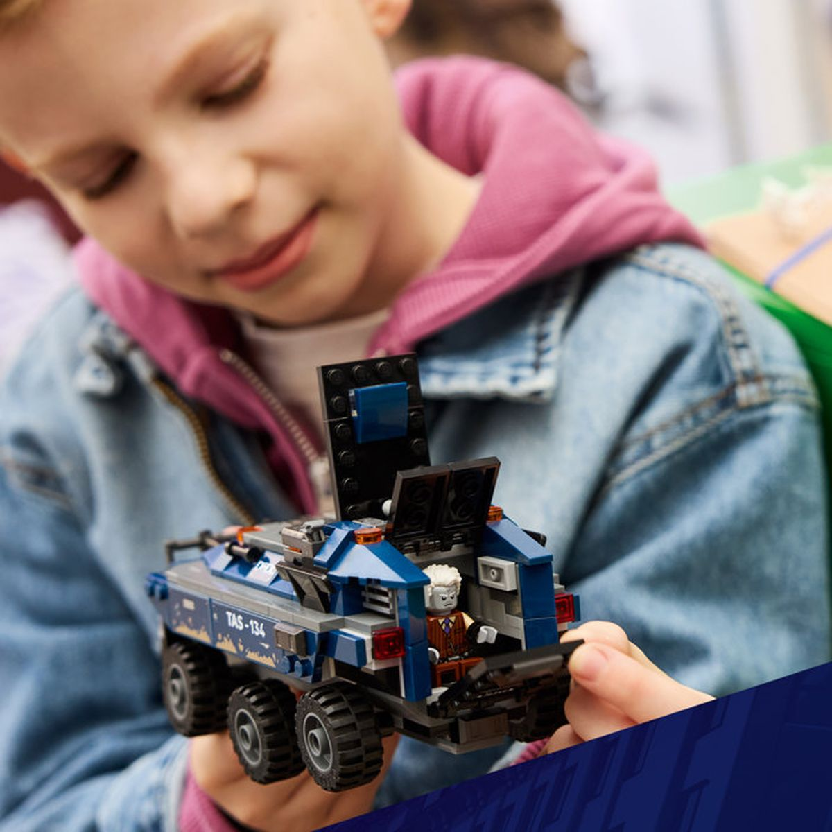 Un bambino gioca con un veicolo LEGO blu con una figura all'interno.