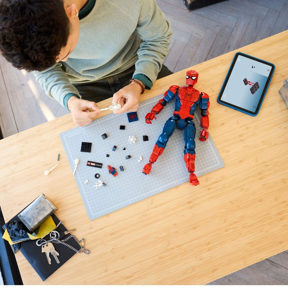 Una persona costruisce una figura di Spiderman con mattoncini Lego. Un tablet mostra le istruzioni.