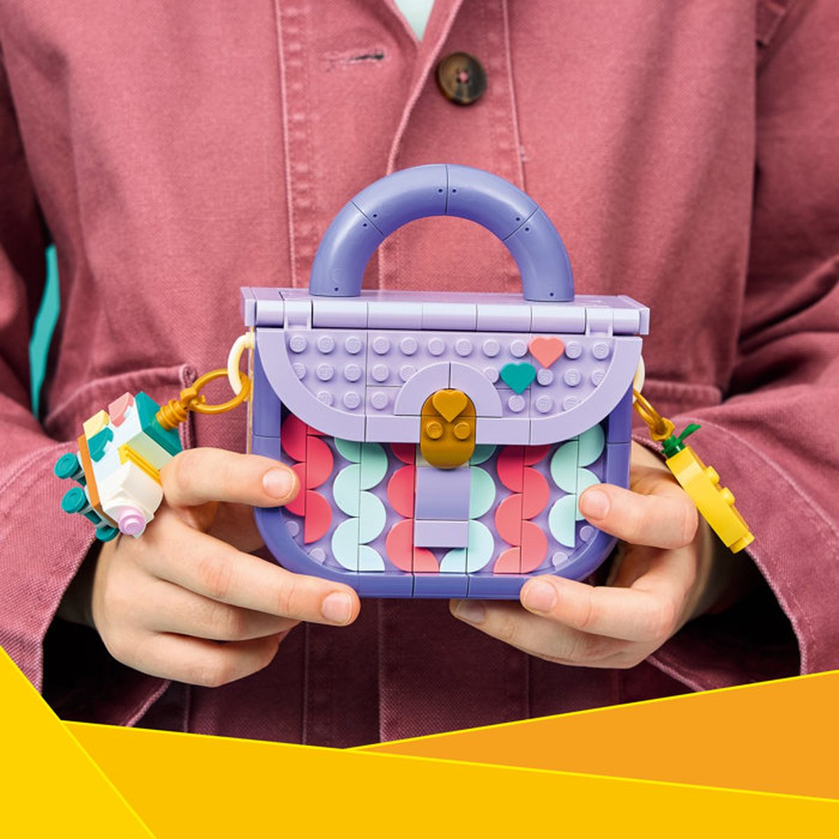 Renkli daire desenli mor Lego çanta, eller tarafından tutuluyor.