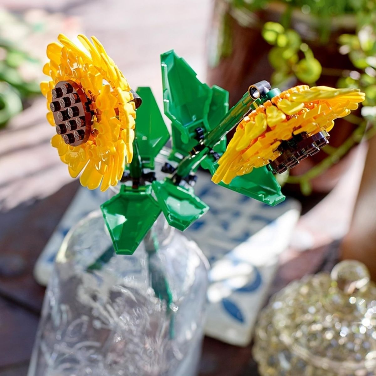 Dos girasoles amarillos de Lego con hojas verdes en un jarrón de cristal.