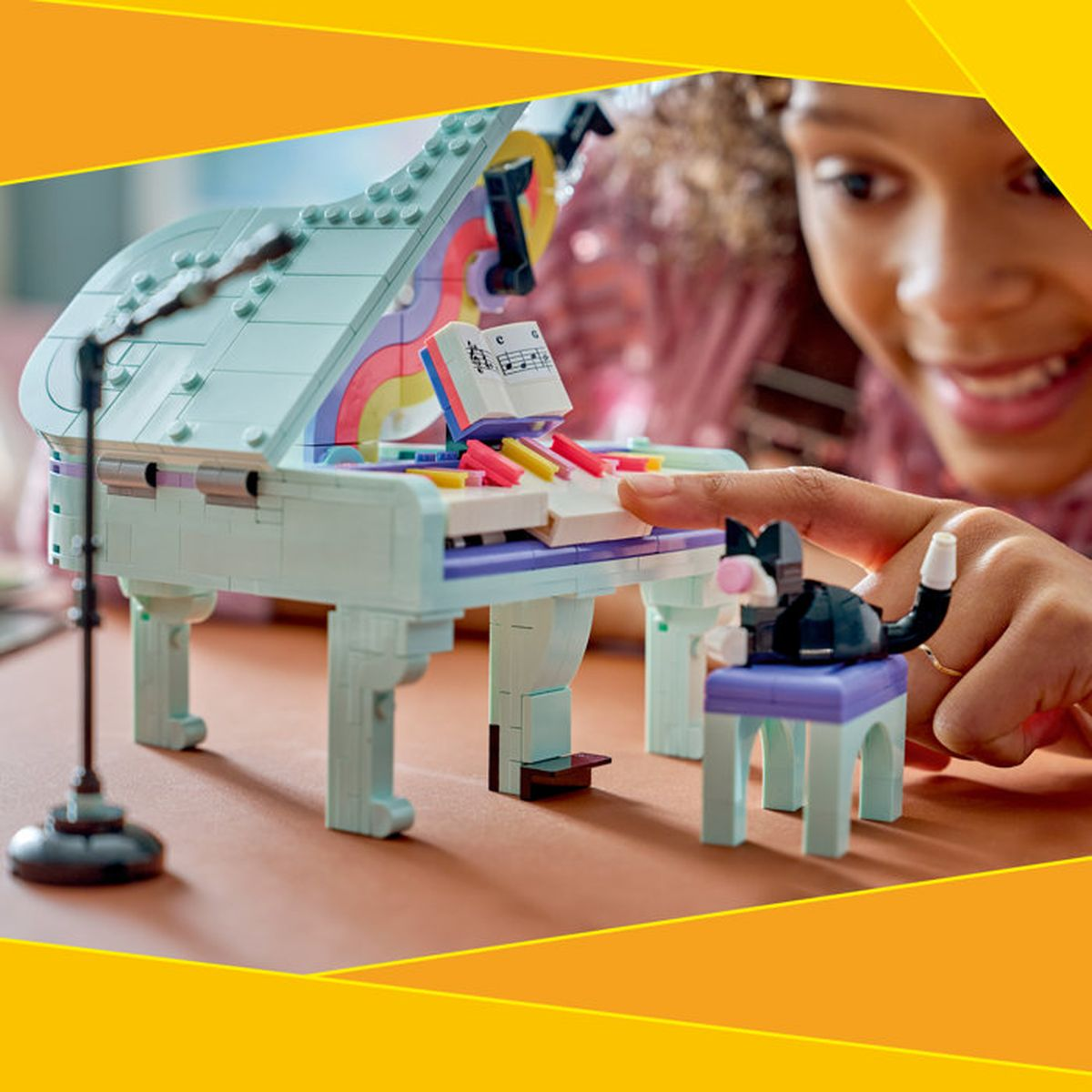 Un piano Lego azul claro con partituras, bolígrafos coloridos y un gato en un taburete.