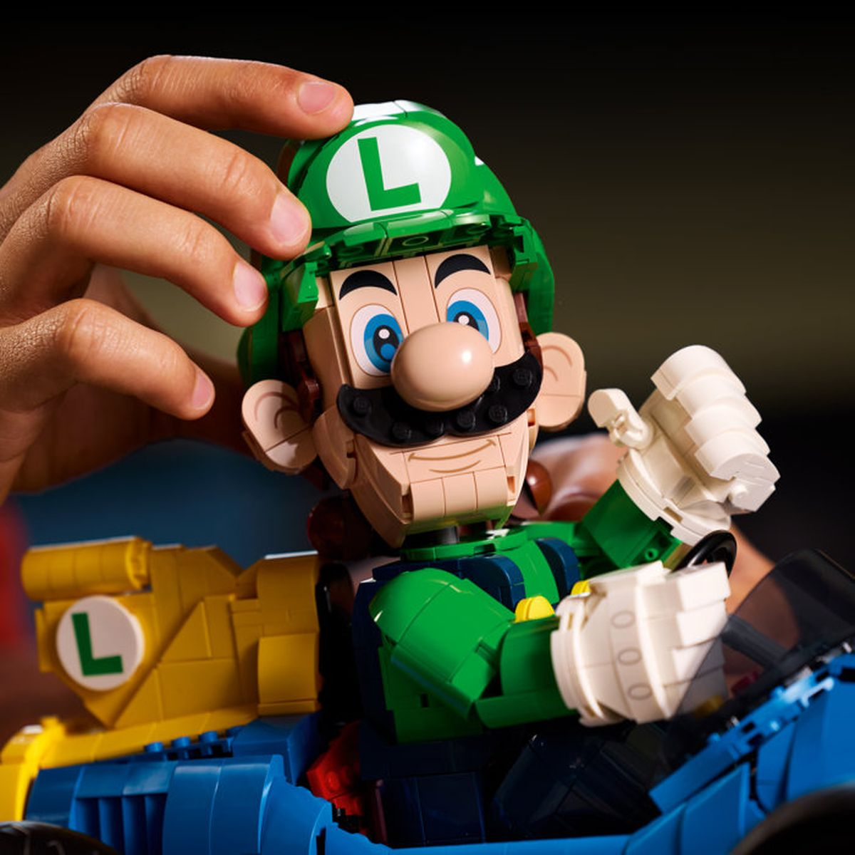 Una figura Lego di Luigi in un go-kart blu assemblata da mani.