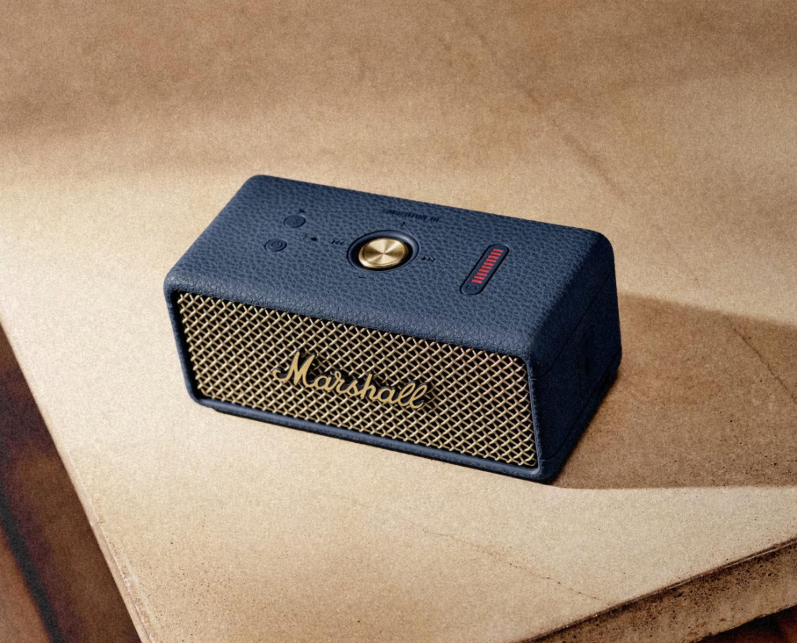 Ein blauer Marshall Lautsprecher mit goldenem Gitter und Bedienelementen auf braunem Untergrund.