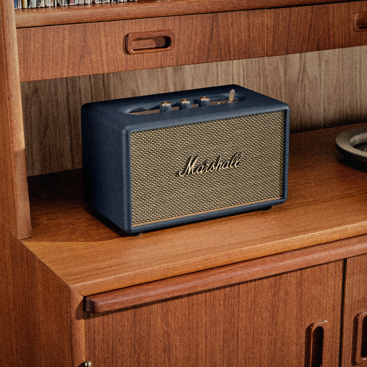 Ein dunkelblauer Marshall-Lautsprecher mit goldenem Gitter auf einem Holzschrank.