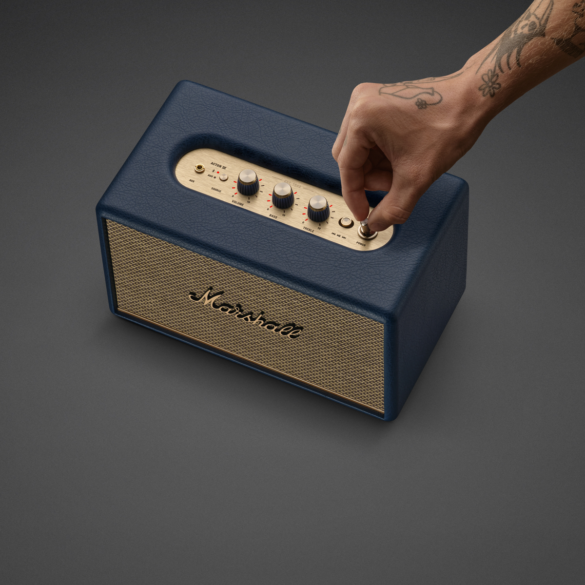 Eine Hand dreht am Knopf eines blauen Marshall-Lautsprechers mit goldenem Gitter.