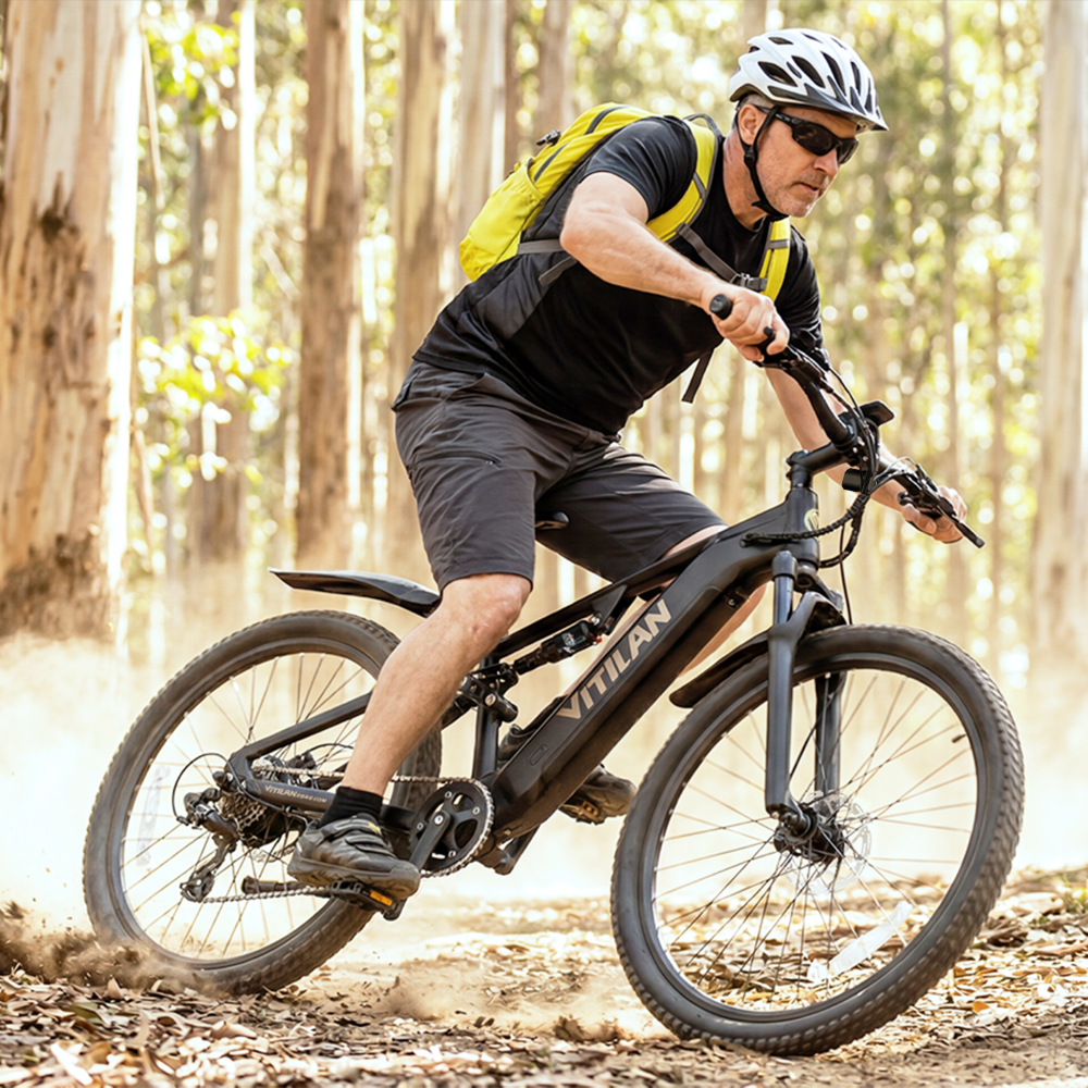 Uomo con casco guida bici elettrica nera su sentiero boschivo.