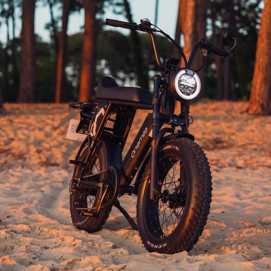 Una bici elettrica nera con pneumatici larghi riposa su una spiaggia sabbiosa.