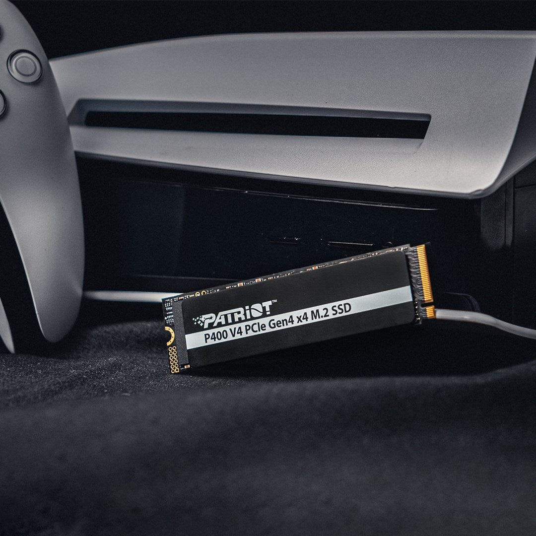 A Patriot M.2 SSD drive rests beside a game console and controller.