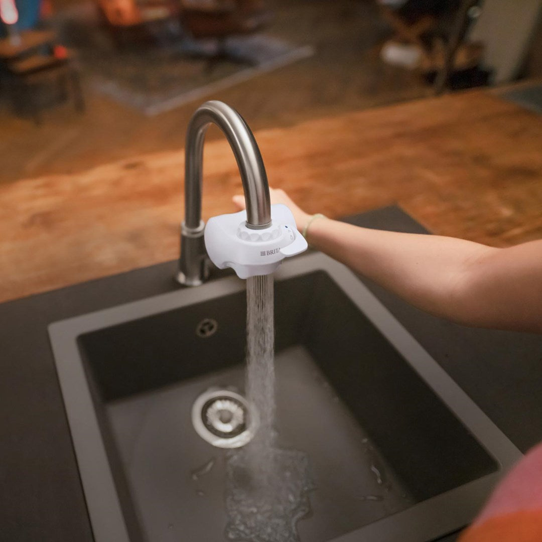 Un rubinetto con filtro Brita bianco che fa scorrere acqua in un lavello scuro.