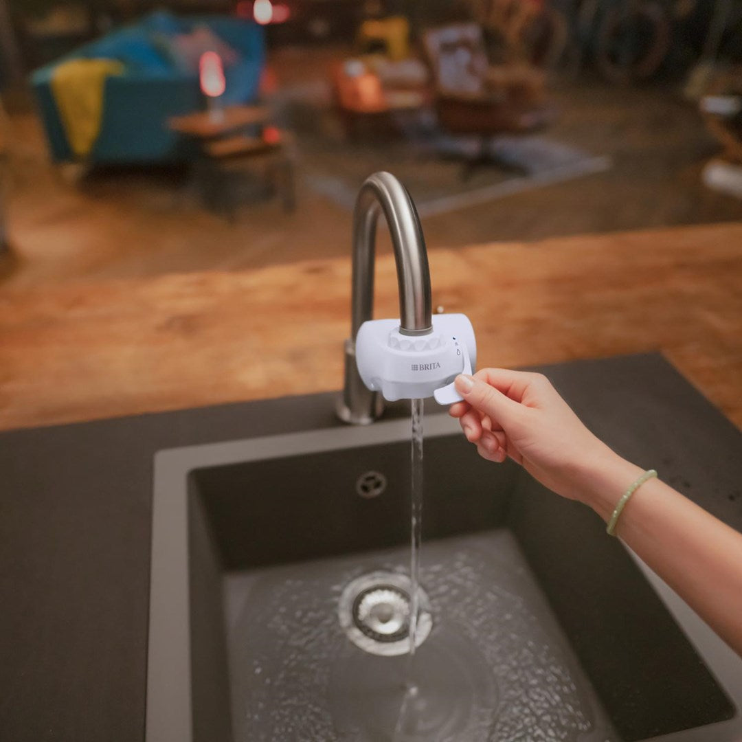 Una mano regola un filtro per l'acqua Brita su un rubinetto mentre l'acqua scorre in un lavello.