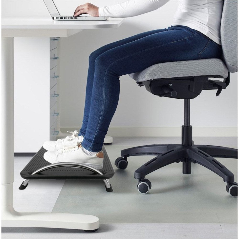 Persona in jeans e sneakers bianche seduta alla scrivania, piedi su poggiapiedi.