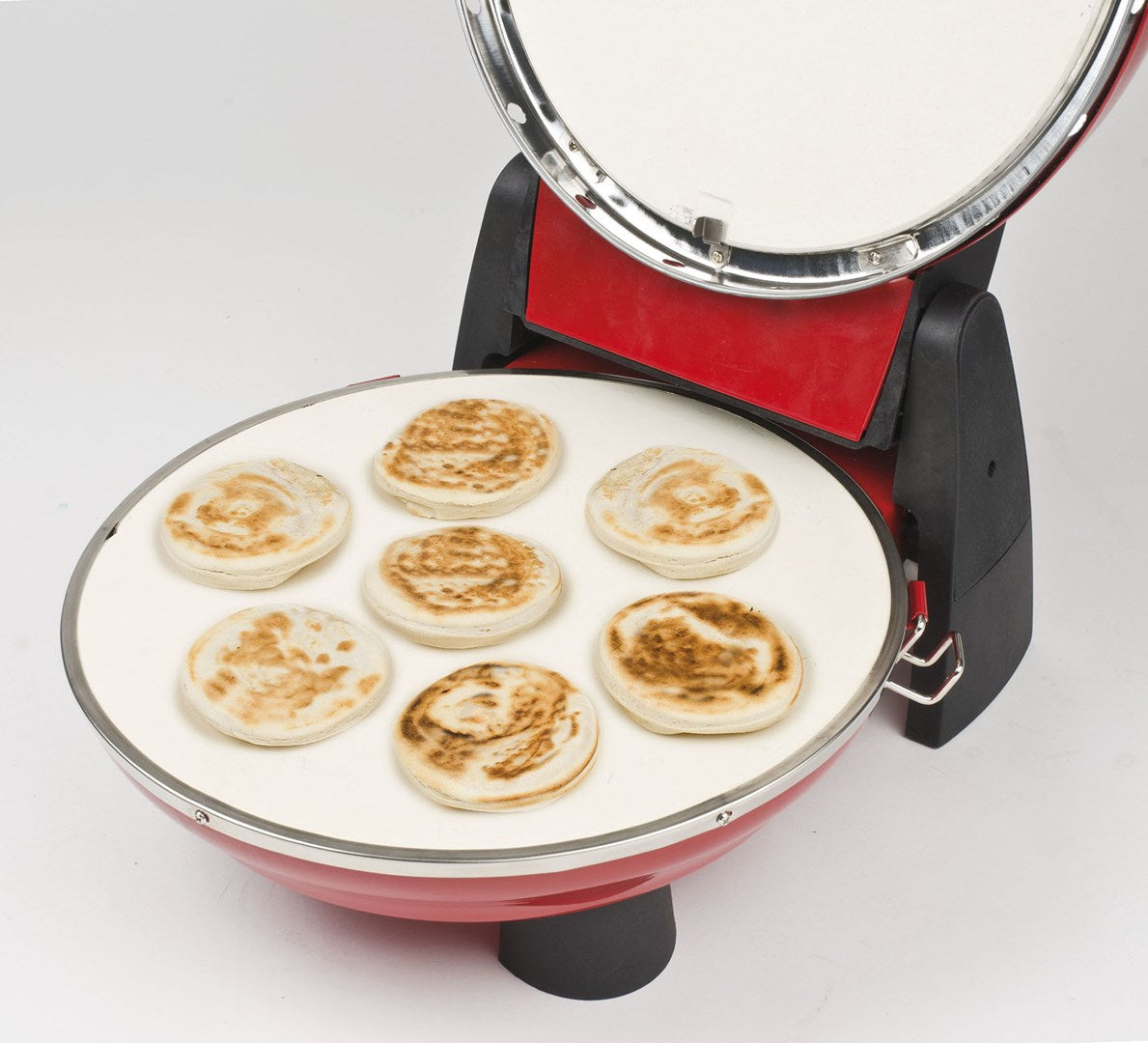 Siete tortitas pequeñas cocinándose en una plancha blanca en una máquina roja.