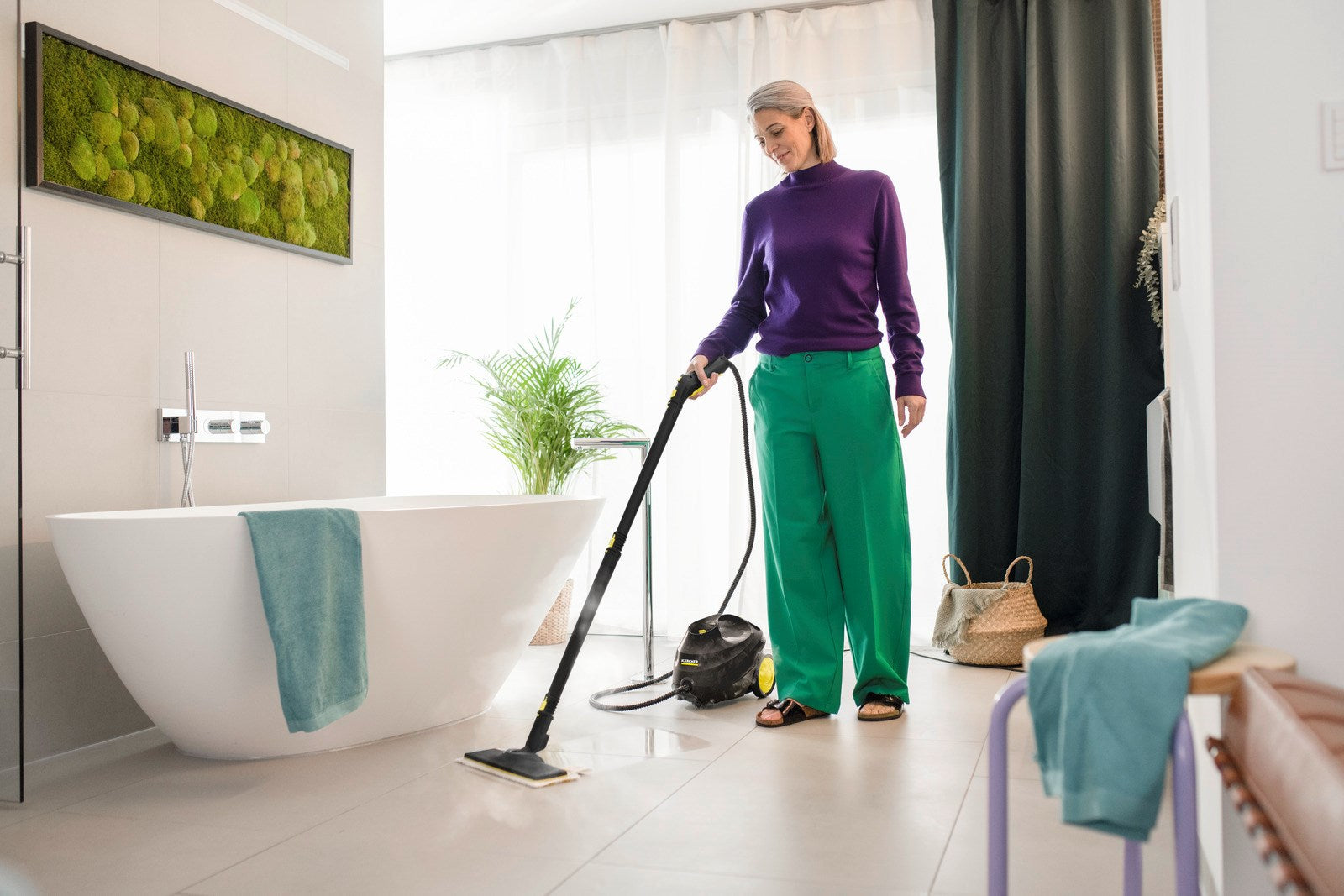 Donna pulisce il pavimento con pulitore a vapore in bagno vicino a vasca freestanding.