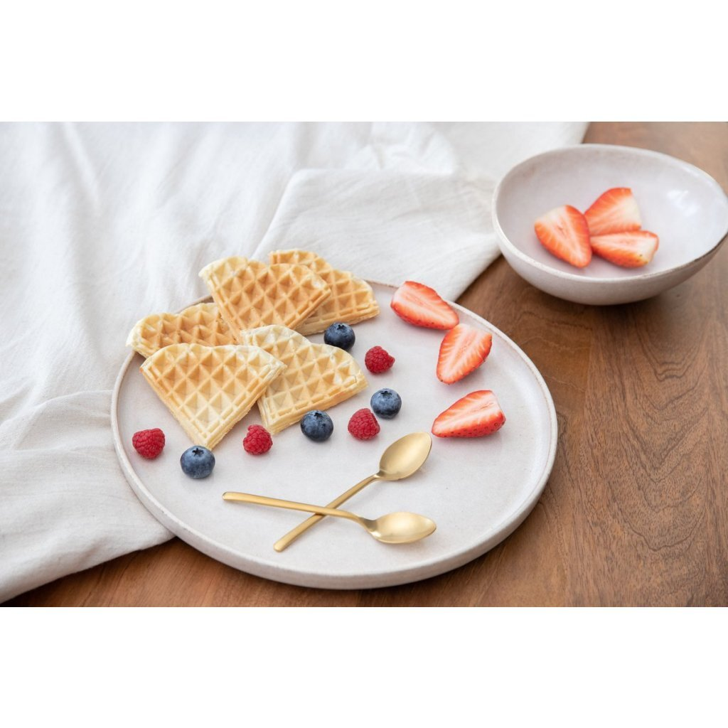 Wafels met bessen en lepels op een bord, met gesneden aardbeien in een kom.