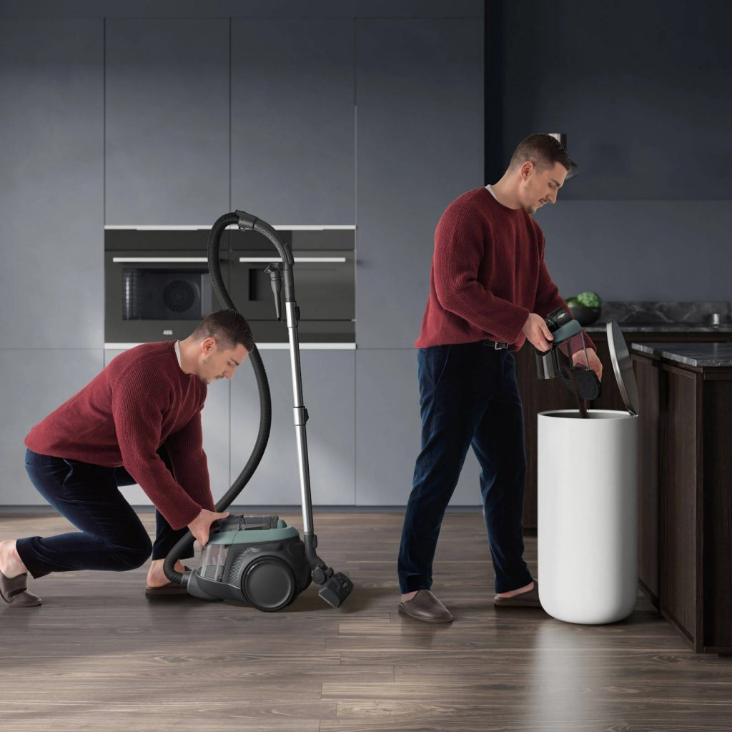 Man with vacuum cleaner in kitchen; man emptying vacuum into bin.