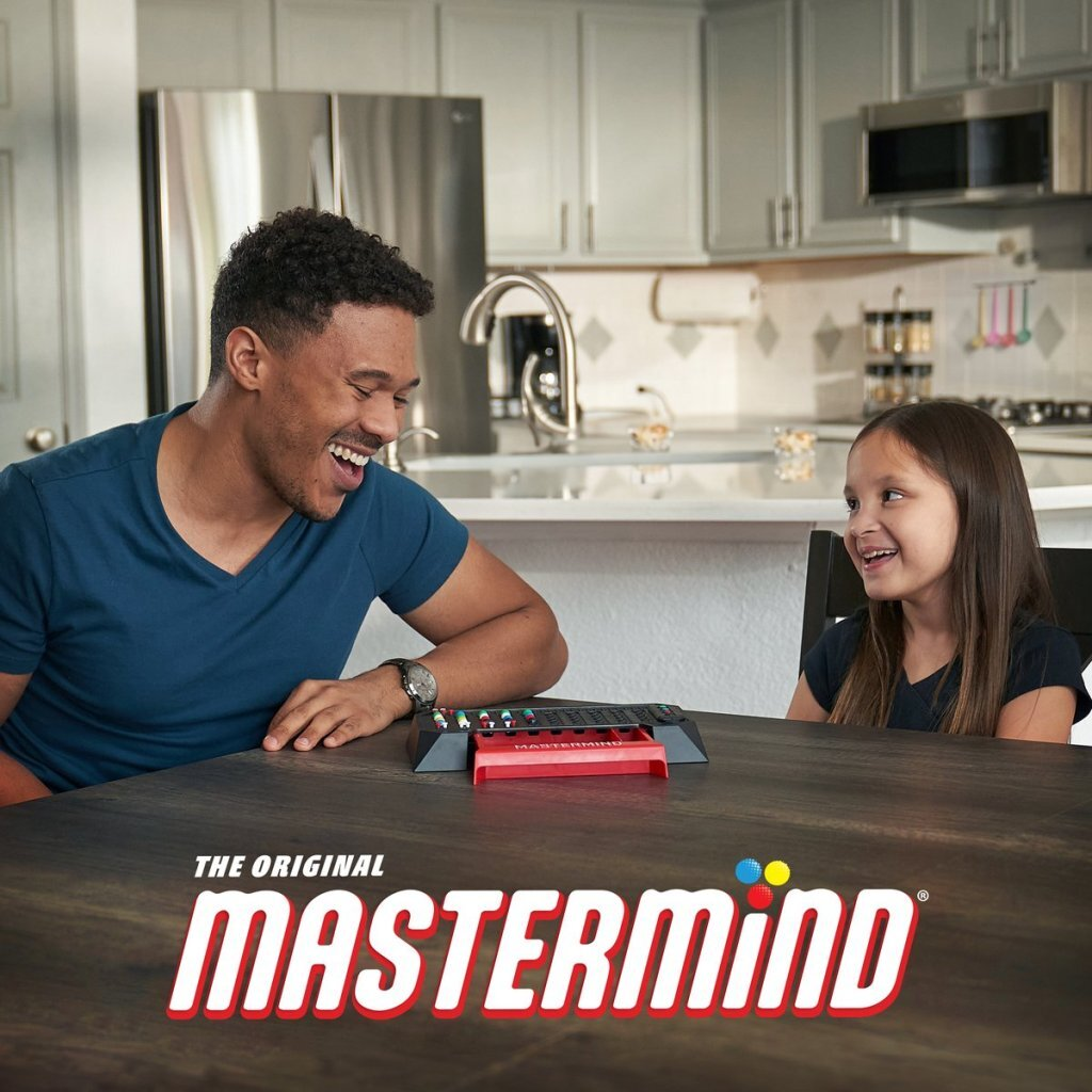 Mann und Mädchen lachen am Tisch, Mastermind-Spiel im Vordergrund.