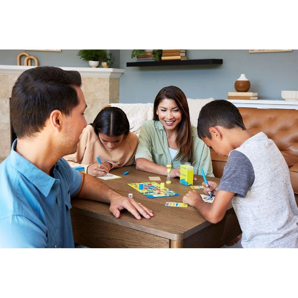 Famiglia gioca a un gioco da tavolo a un tavolo. Bambini e genitori scrivono e ridono.