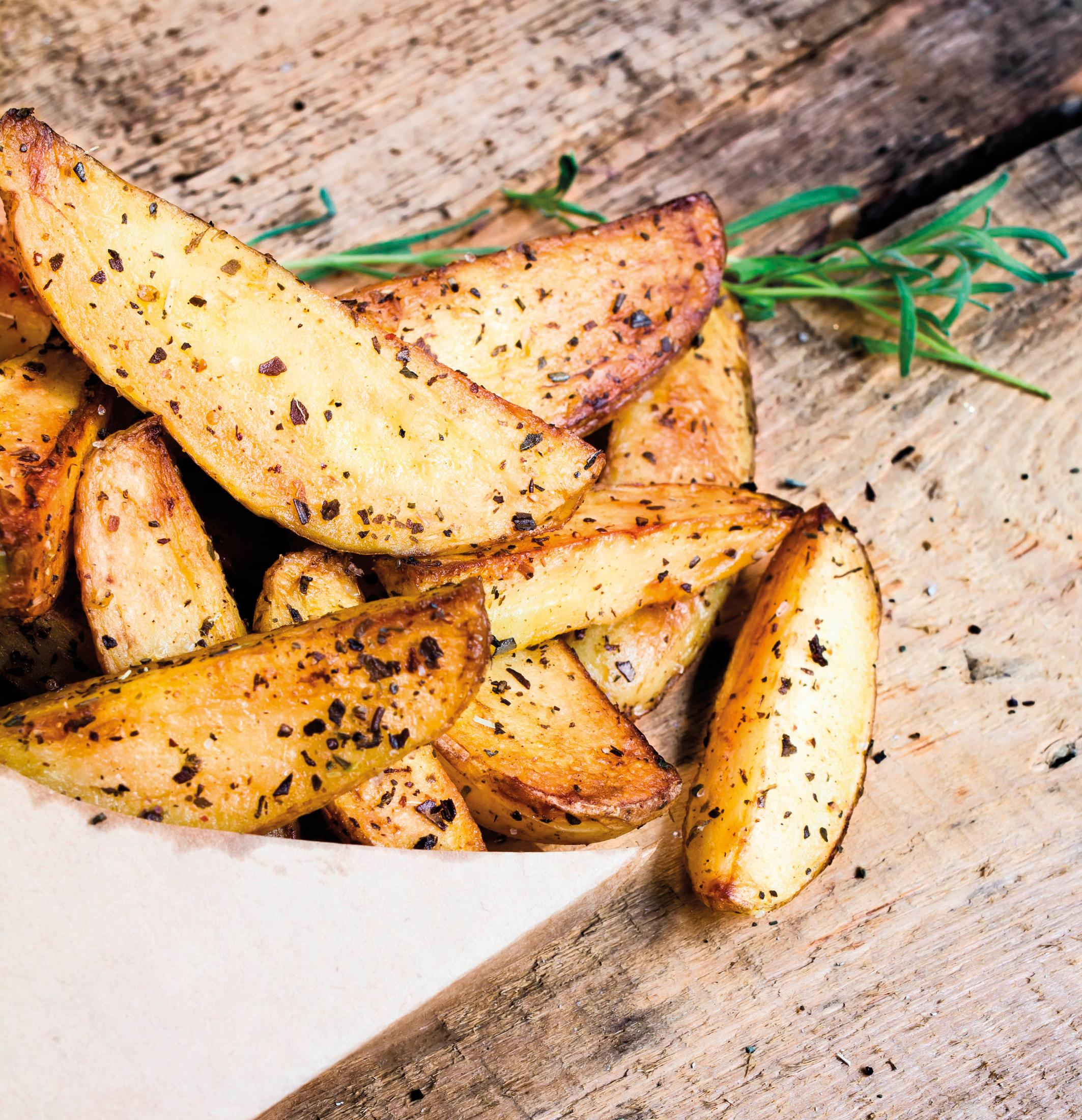 Spicchi di patate dorati con erbe aromatiche su superficie di legno.