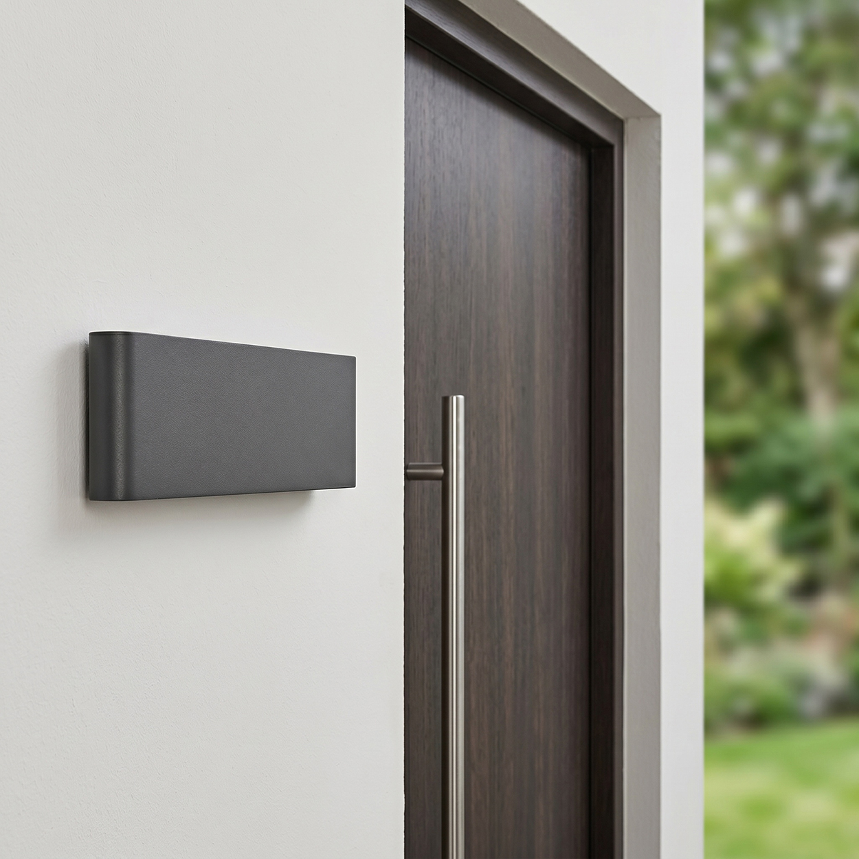Grauer Briefkasten an weißer Wand neben dunkler Holztür mit Edelstahlgriff.