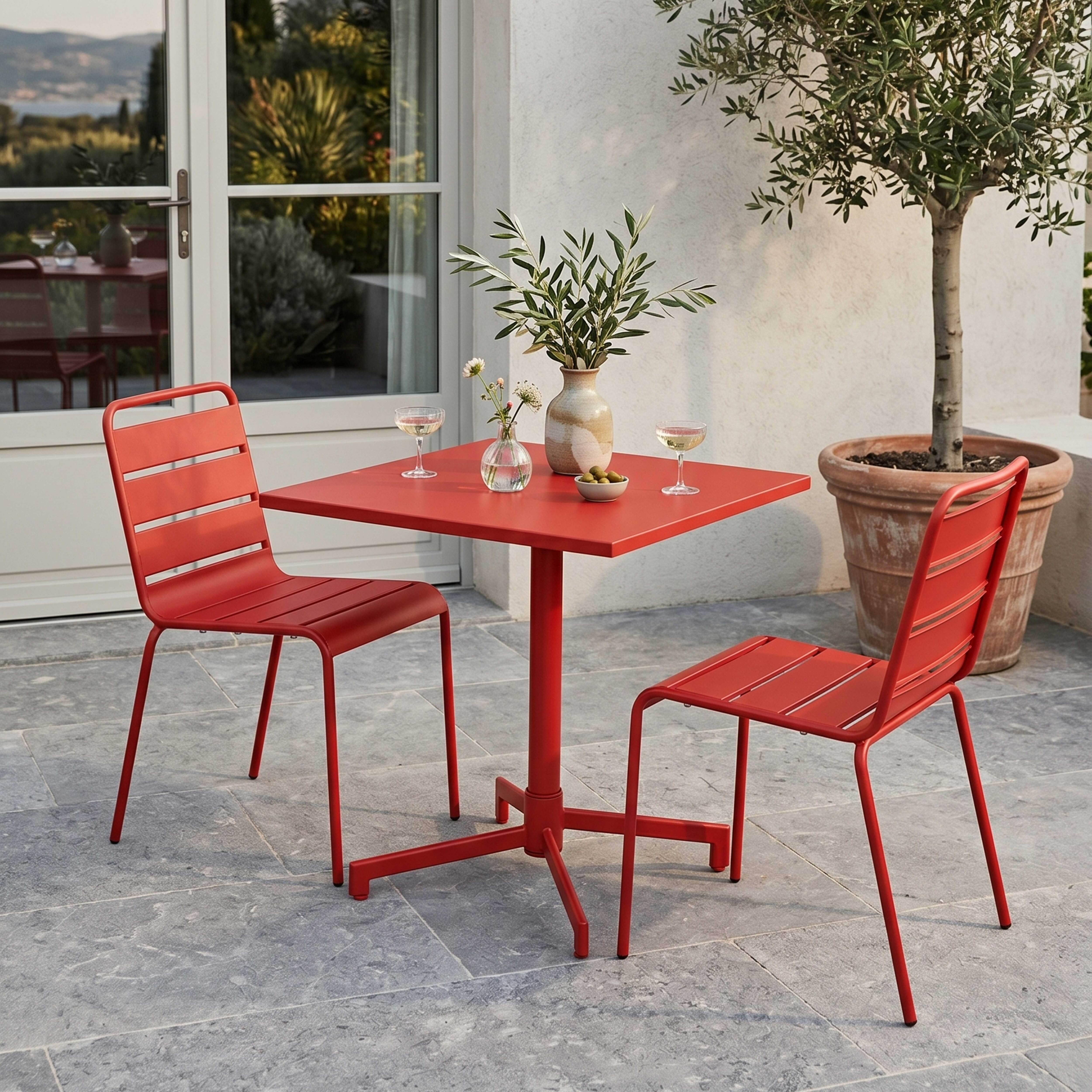 Roter Tisch mit zwei Stühlen, Gläsern, Vase und Oliven im Freien.