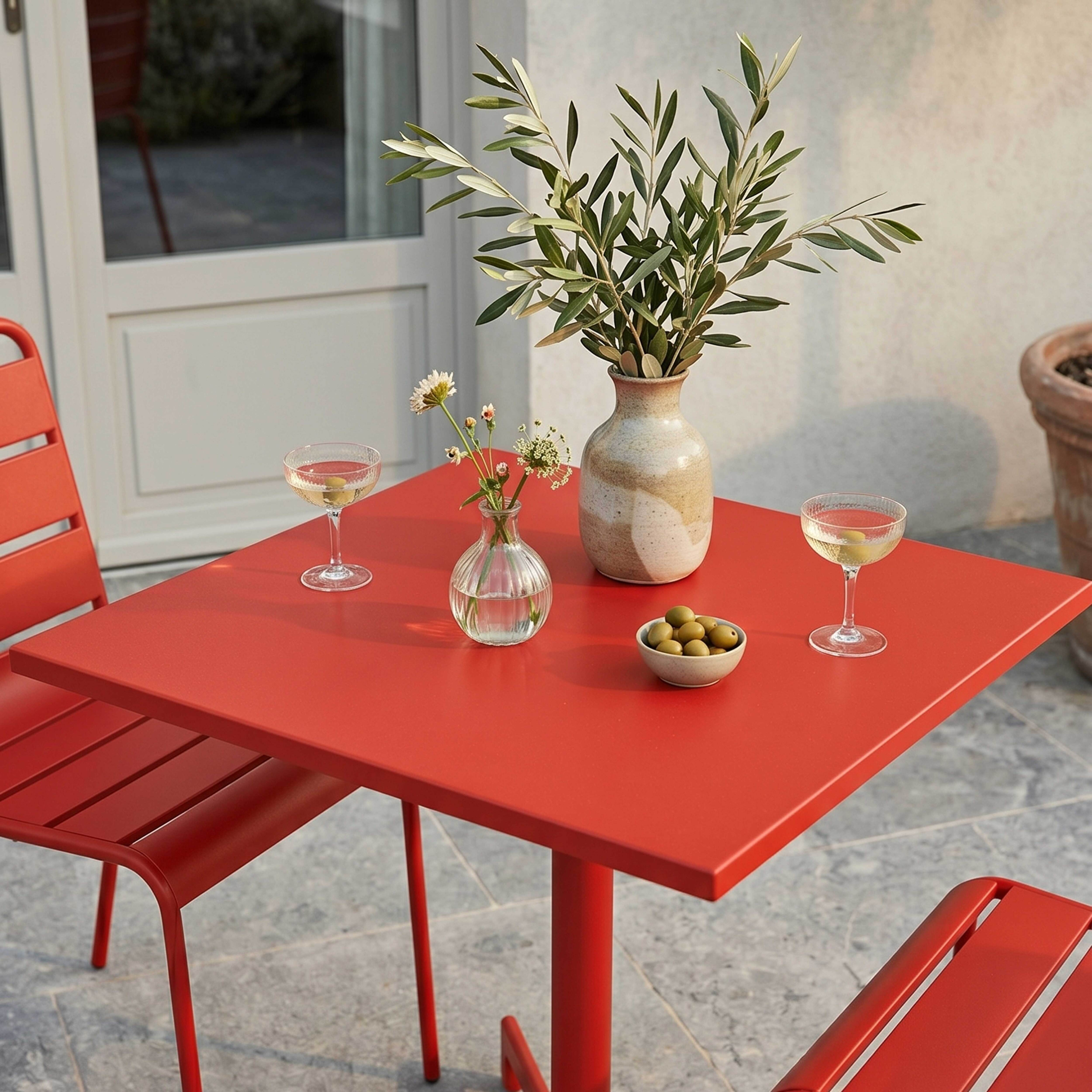 Ein roter Tisch mit Gläsern, Oliven und Blumen im Freien.