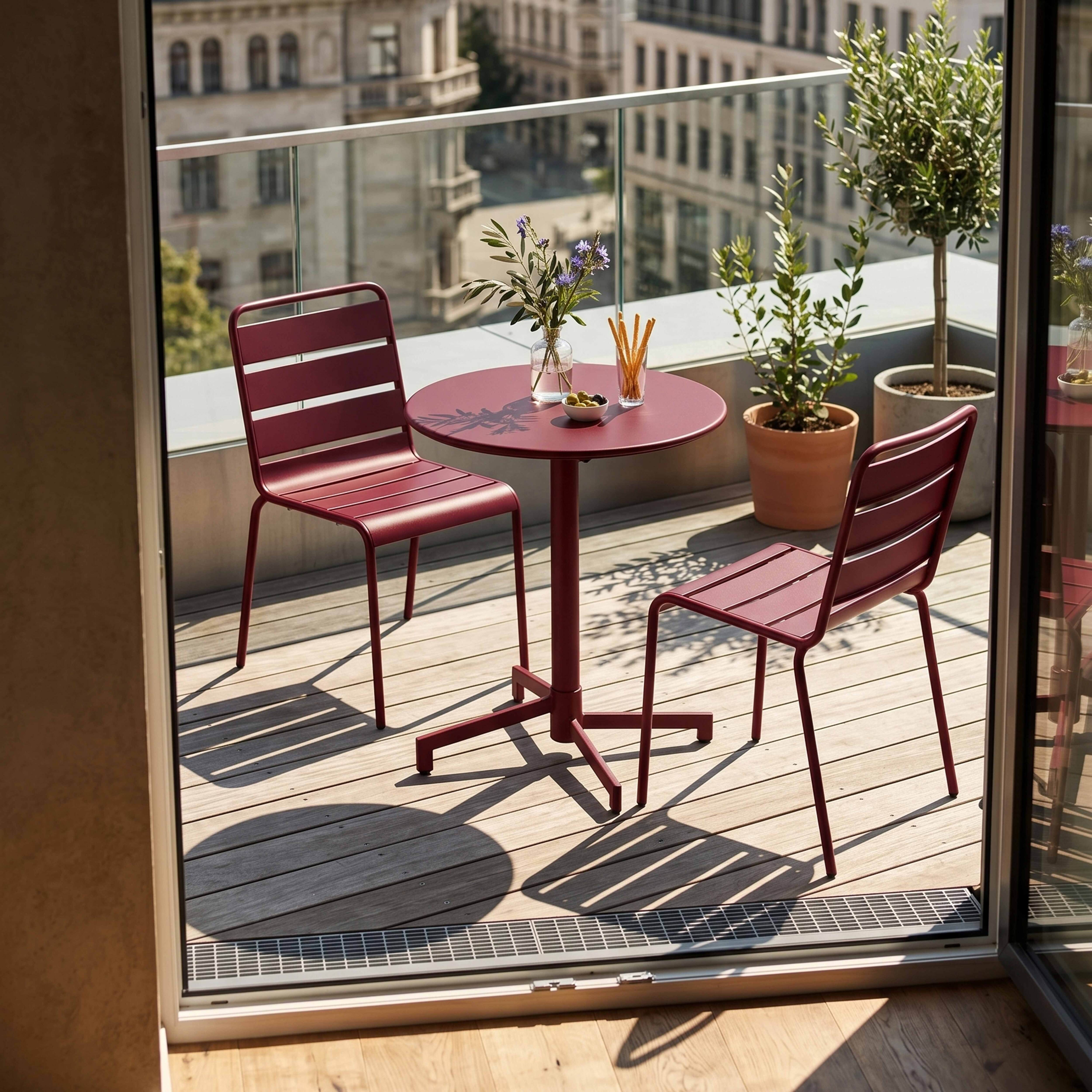 Rote Metallgarnitur auf einem Balkon mit Holzboden, Blick auf Stadtgebäude.