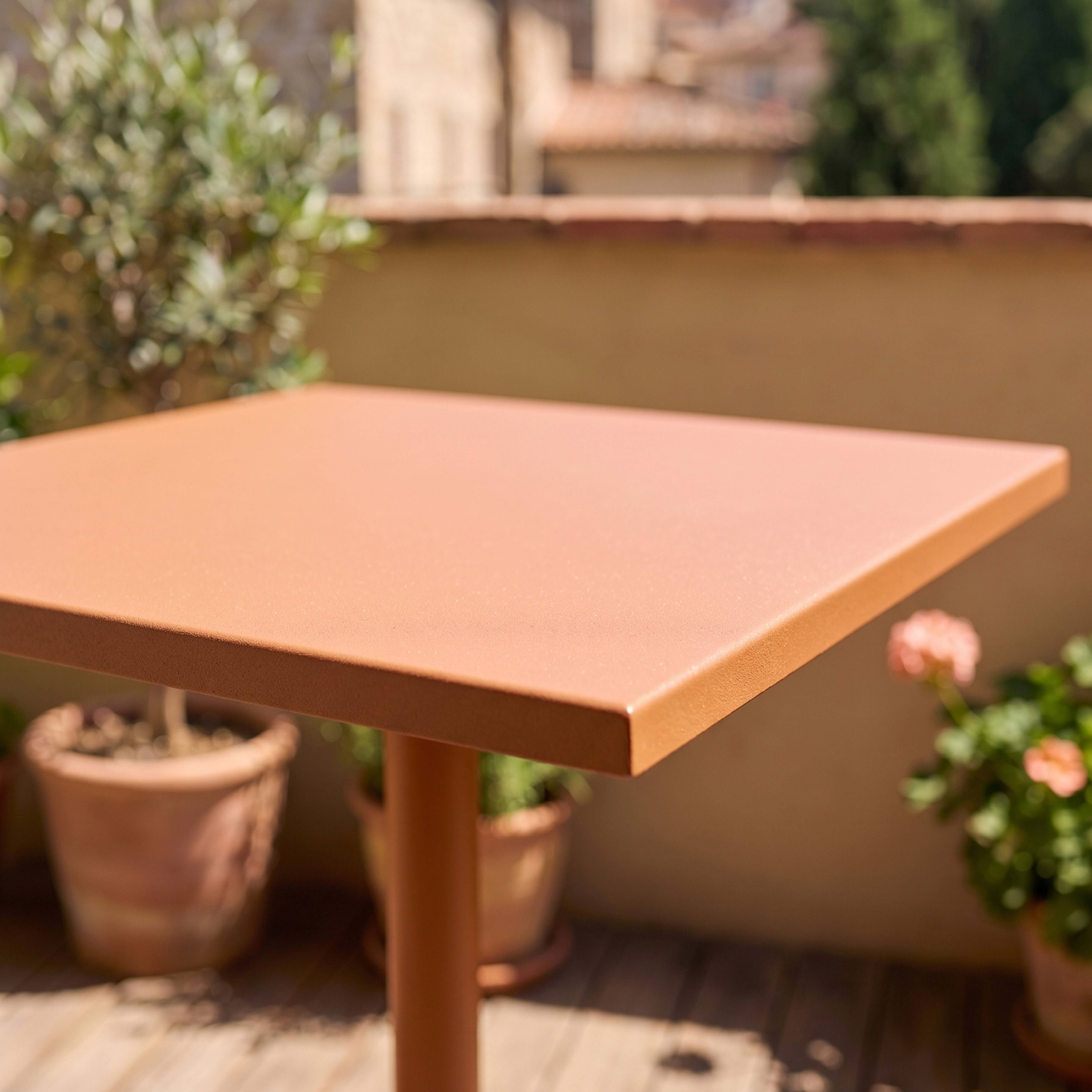 Ein korallenfarbener Tisch mit einem Fuß auf einer Holzterrasse, umgeben von Pflanzen.