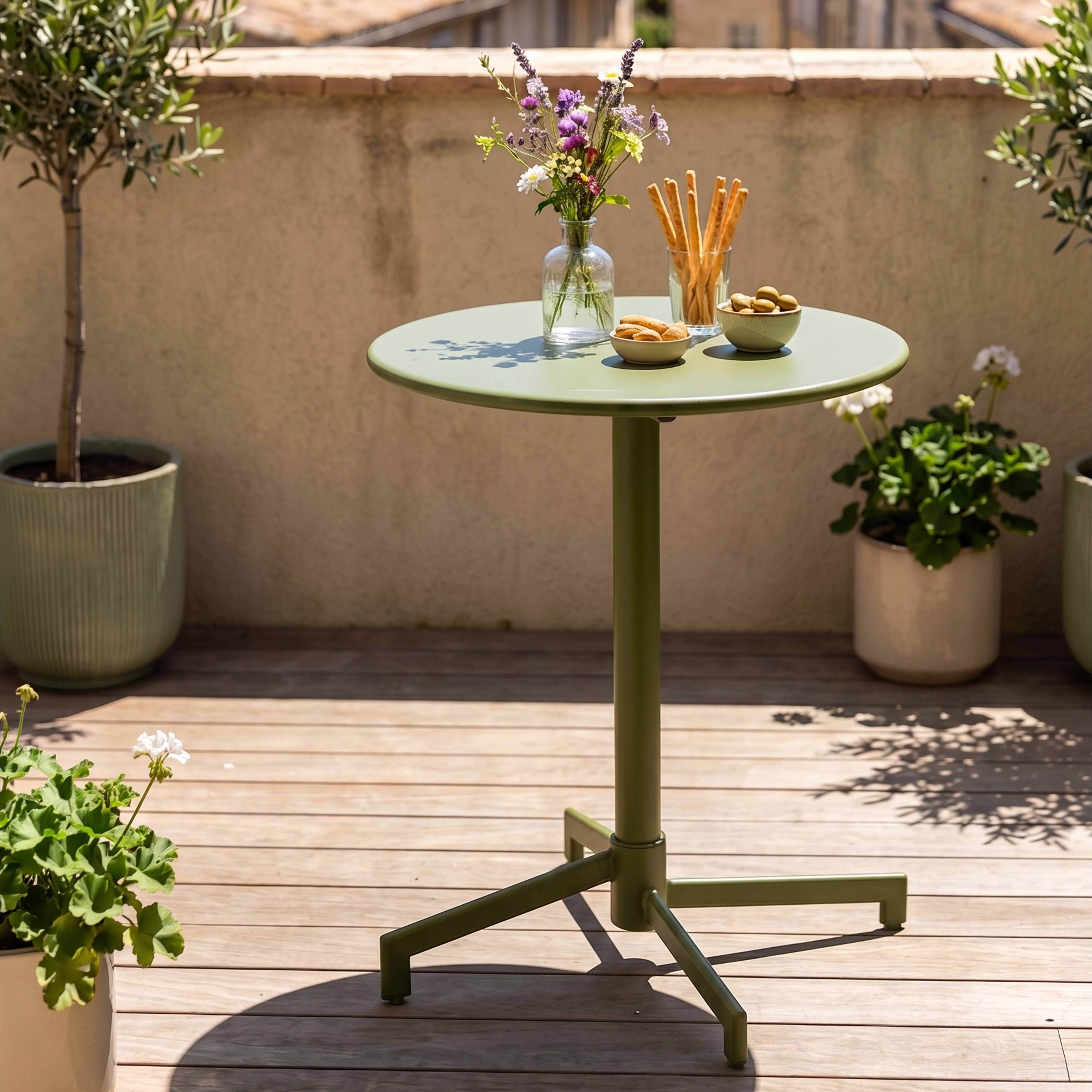 Ein grüner Tisch mit Blumen, Keksen und Oliven auf einer Holzterrasse.