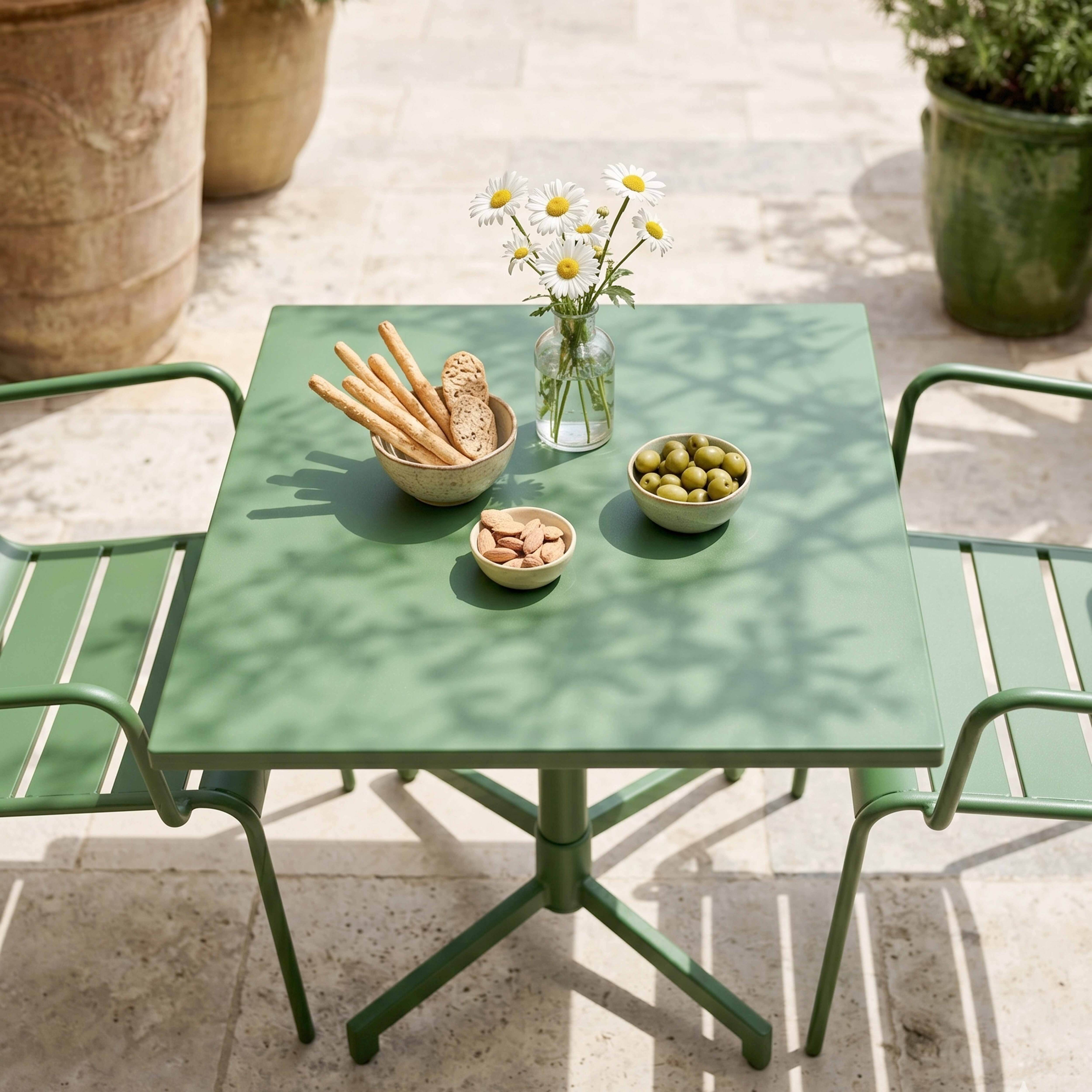 Grüner Tisch mit Snacks und Blumen im Freien. Zwei Stühle stehen daneben.