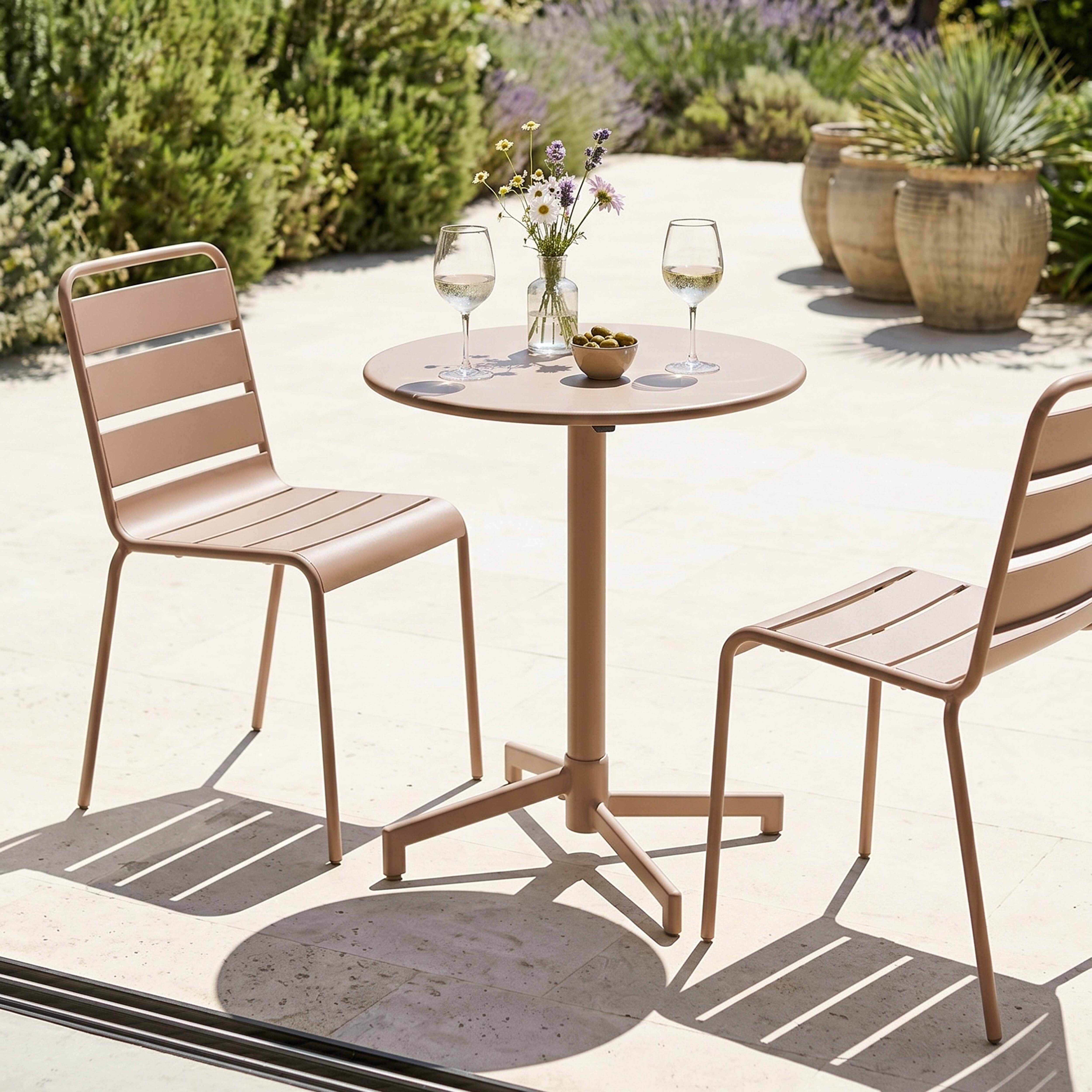 Ein runder Tisch mit zwei Stühlen in einem Garten, mit Blumen und Oliven.