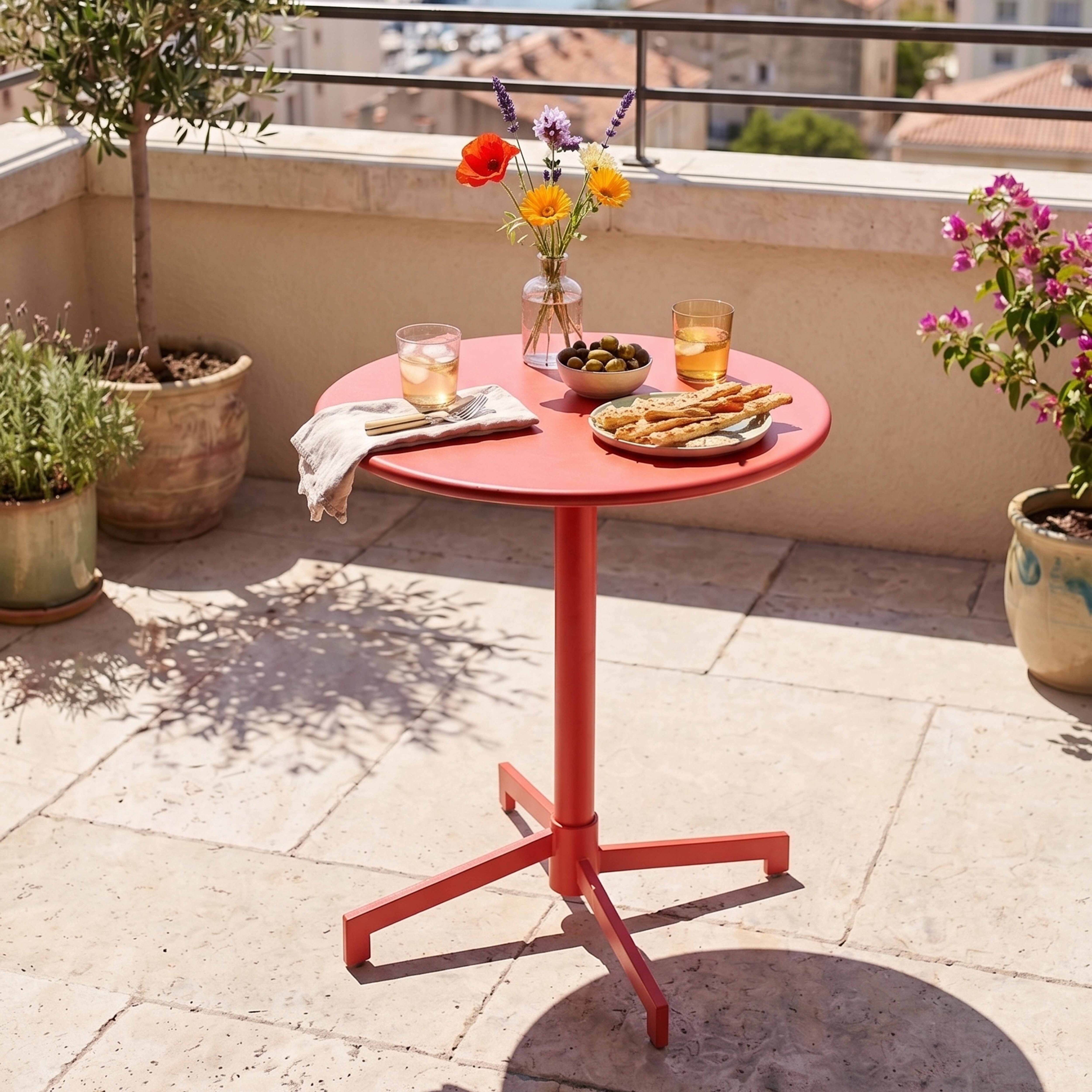 Roter Tisch mit Blumen, Oliven, Brot und Getränken auf einer Terrasse.