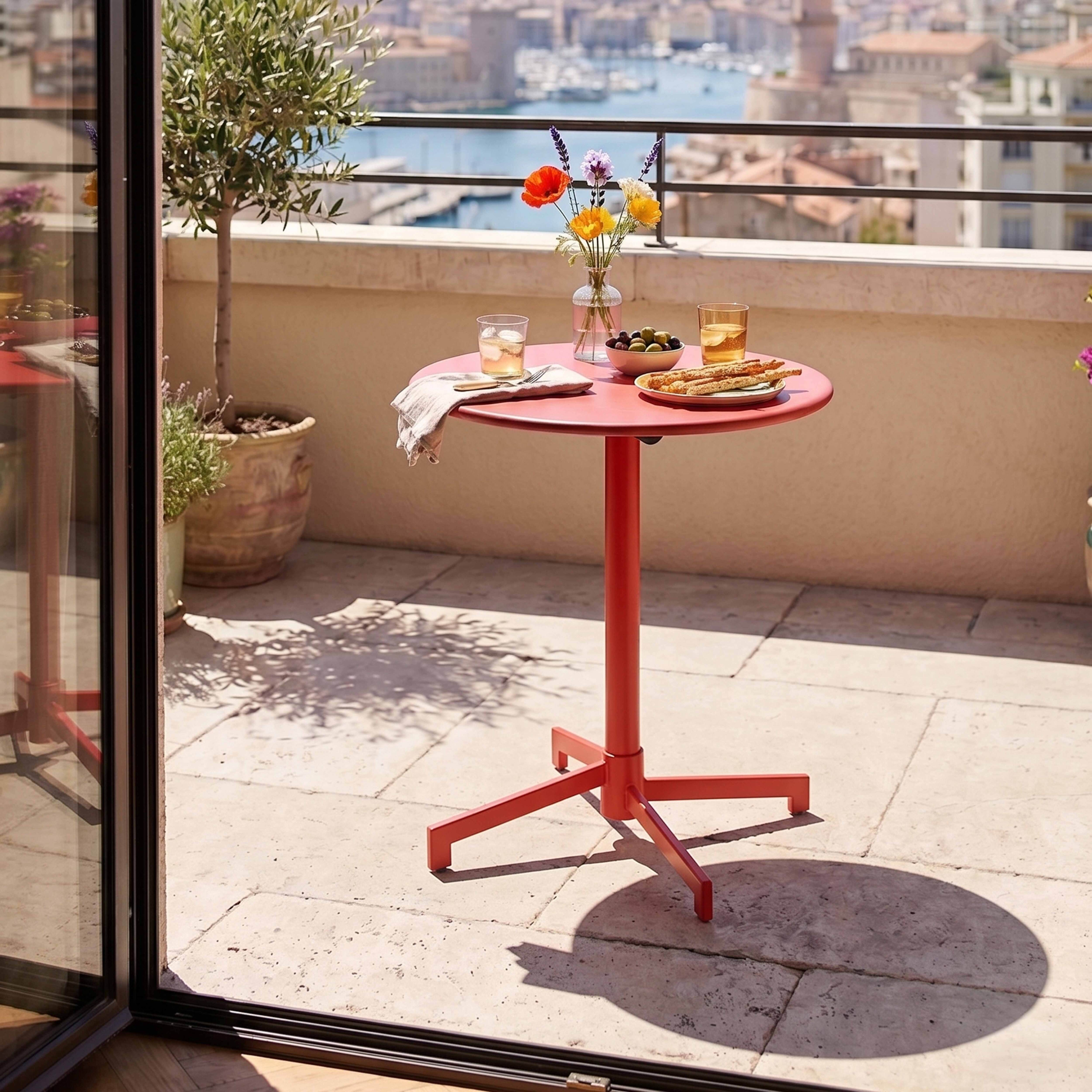 Ein roter Tisch auf einer Terrasse mit Blick auf eine Stadt am Wasser.