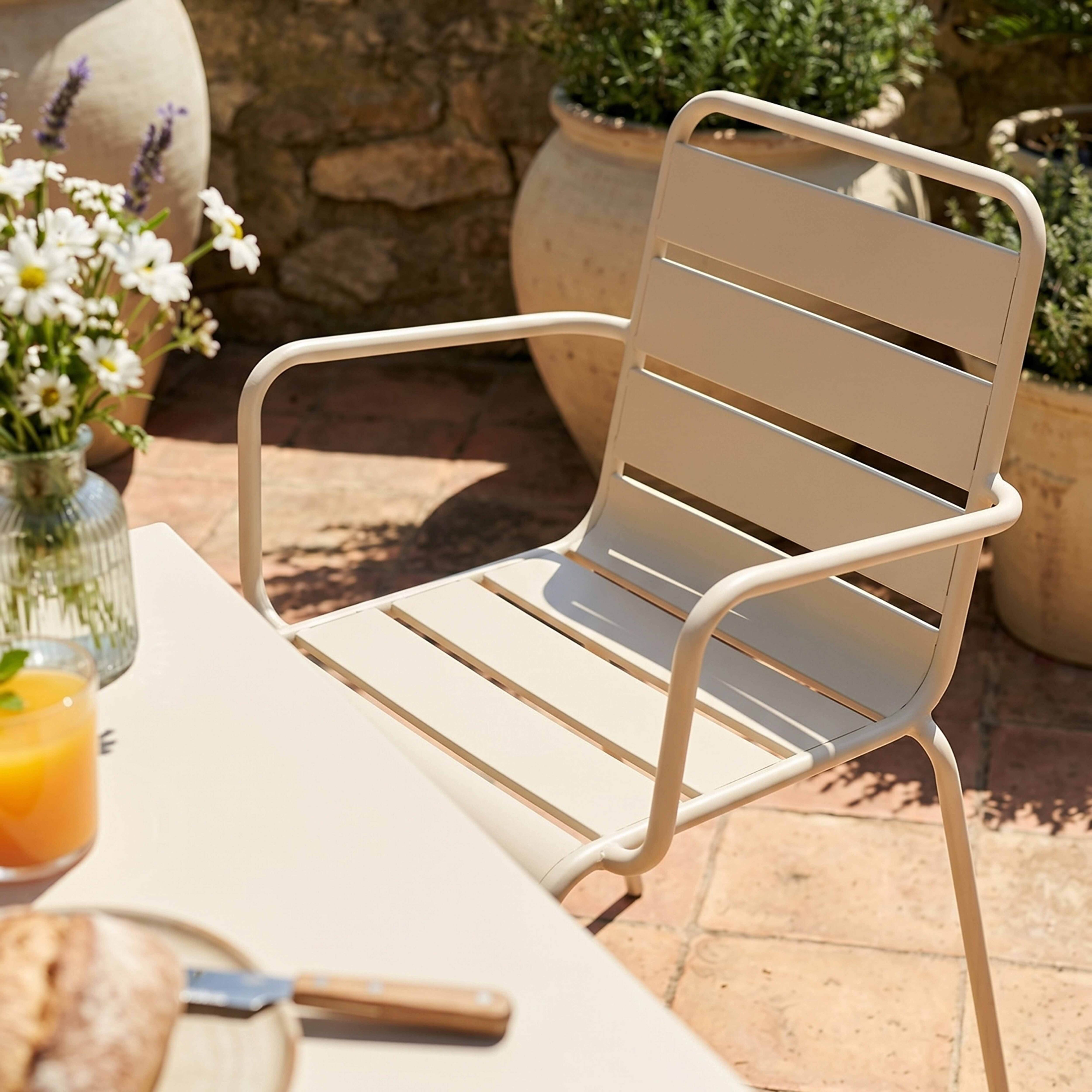 Eine helle Gartenstuhl vor einem Steintisch mit Blumen und Saft.