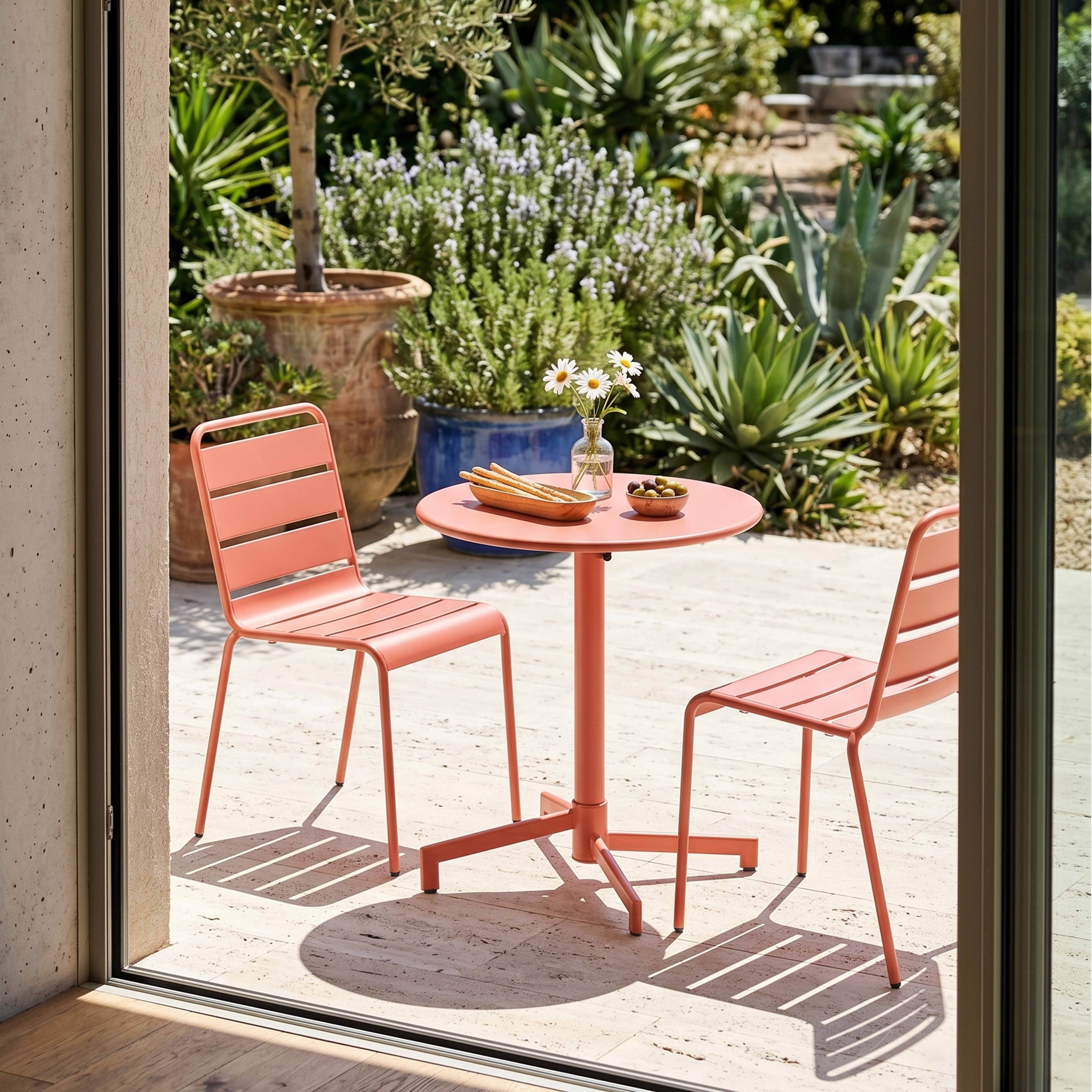 Zwei Korallenstühle und ein Tisch mit Brotstangen und Oliven im Garten.