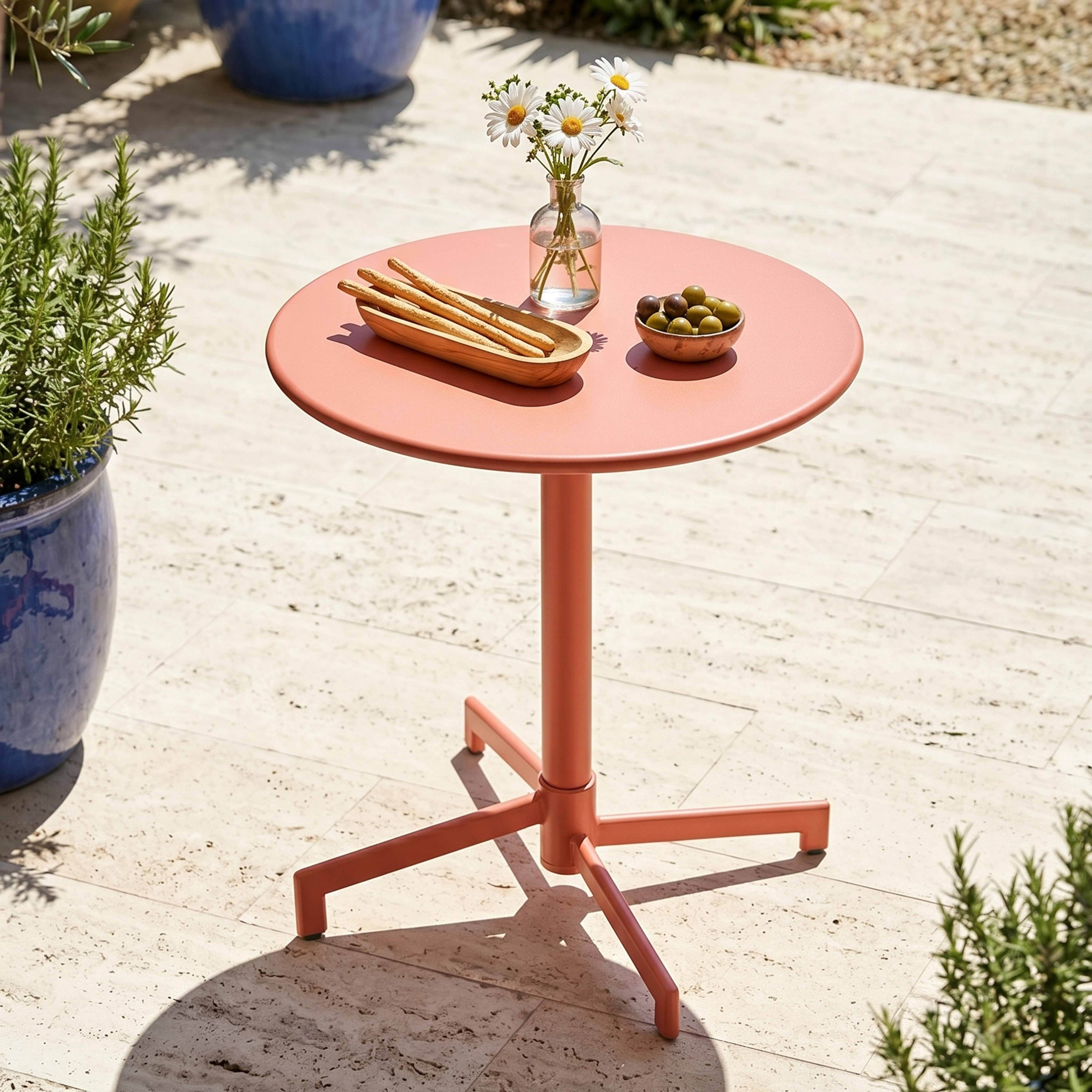 Ein rosafarbener Tisch mit Blumen, Brot und Oliven steht auf einer Terrasse.