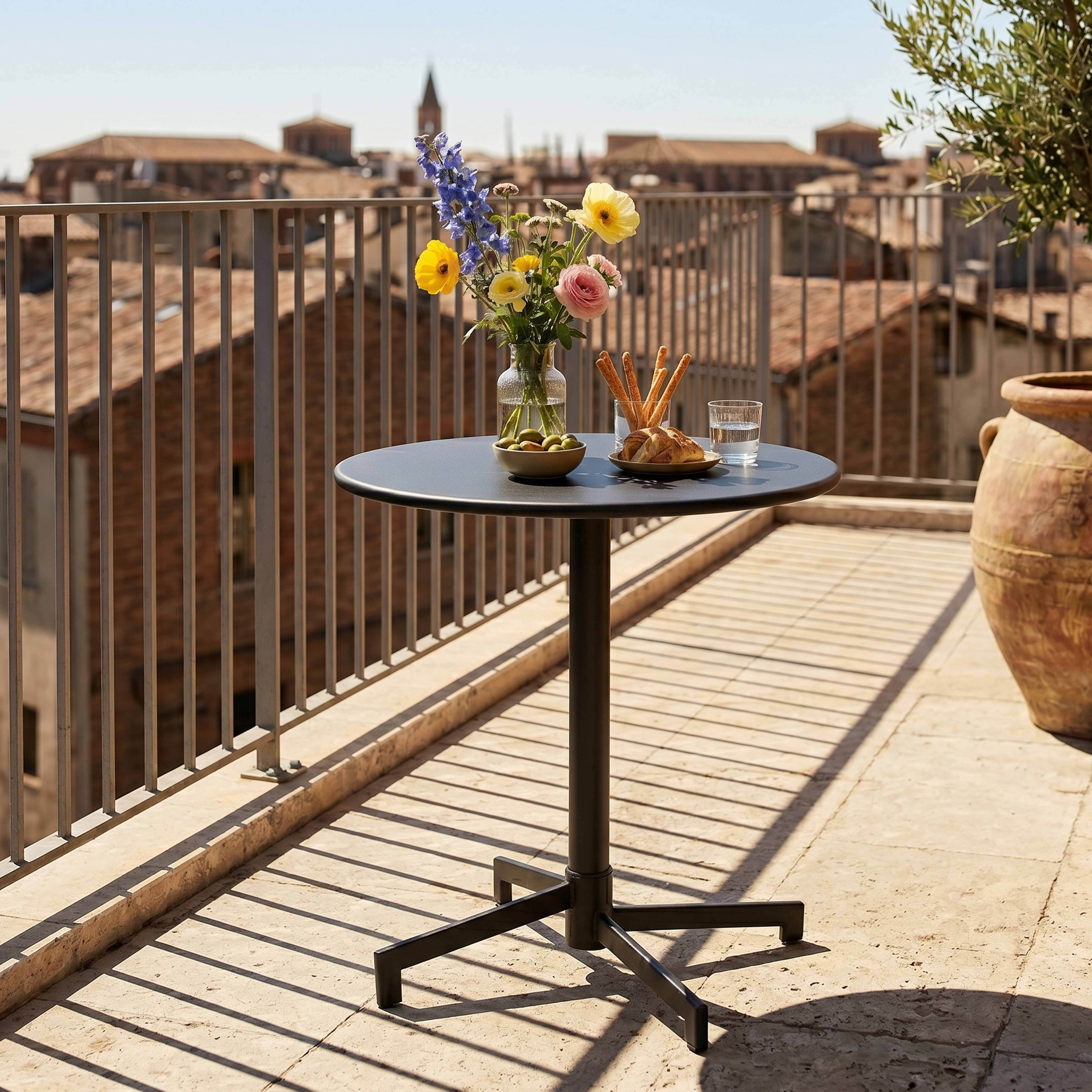 Ein runder Tisch mit Blumen, Oliven und Brot auf einer Terrasse mit Blick auf Gebäude.