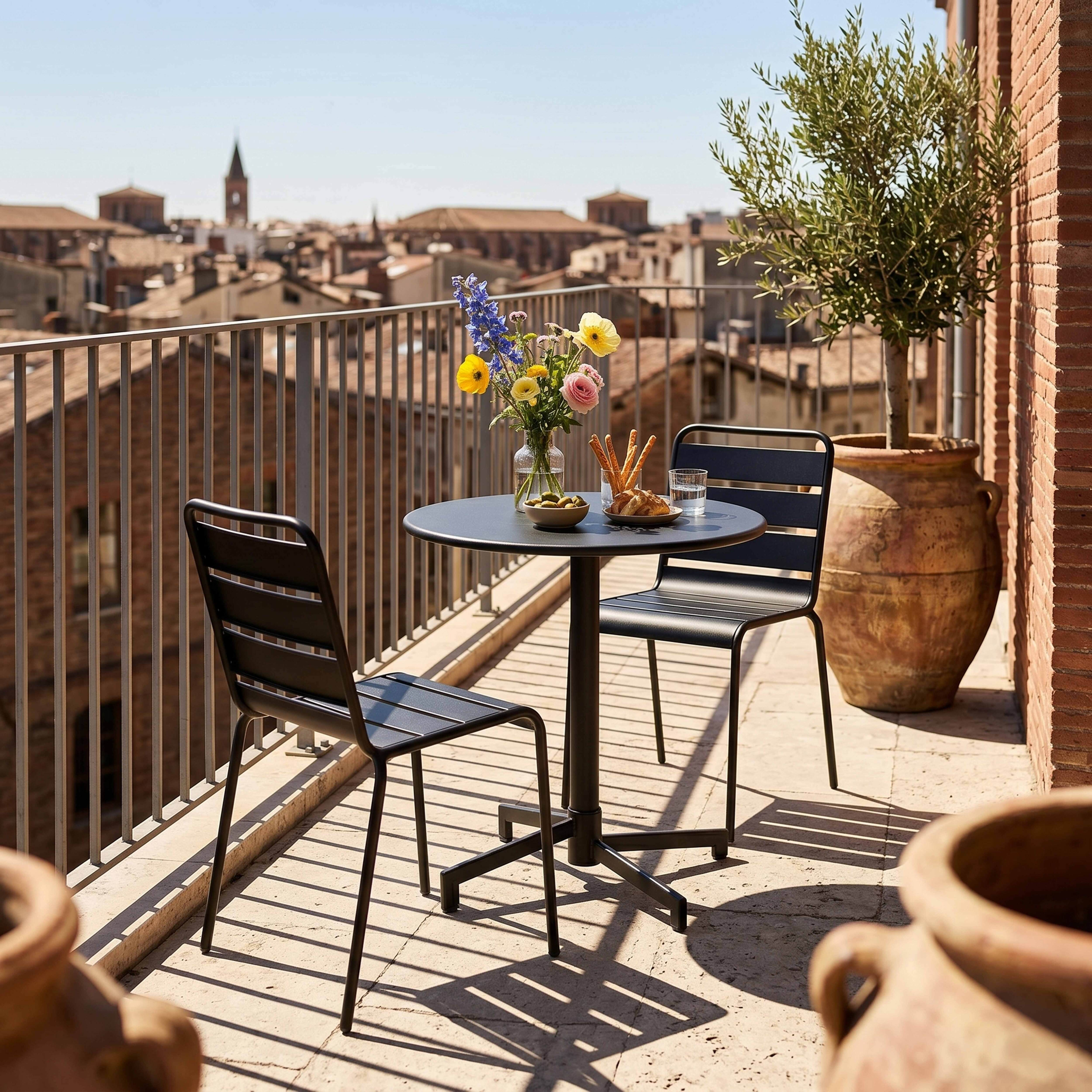 Ein kleiner Tisch mit Blumen, Oliven und Brot steht auf einem Balkon mit Blick auf eine Stadt.